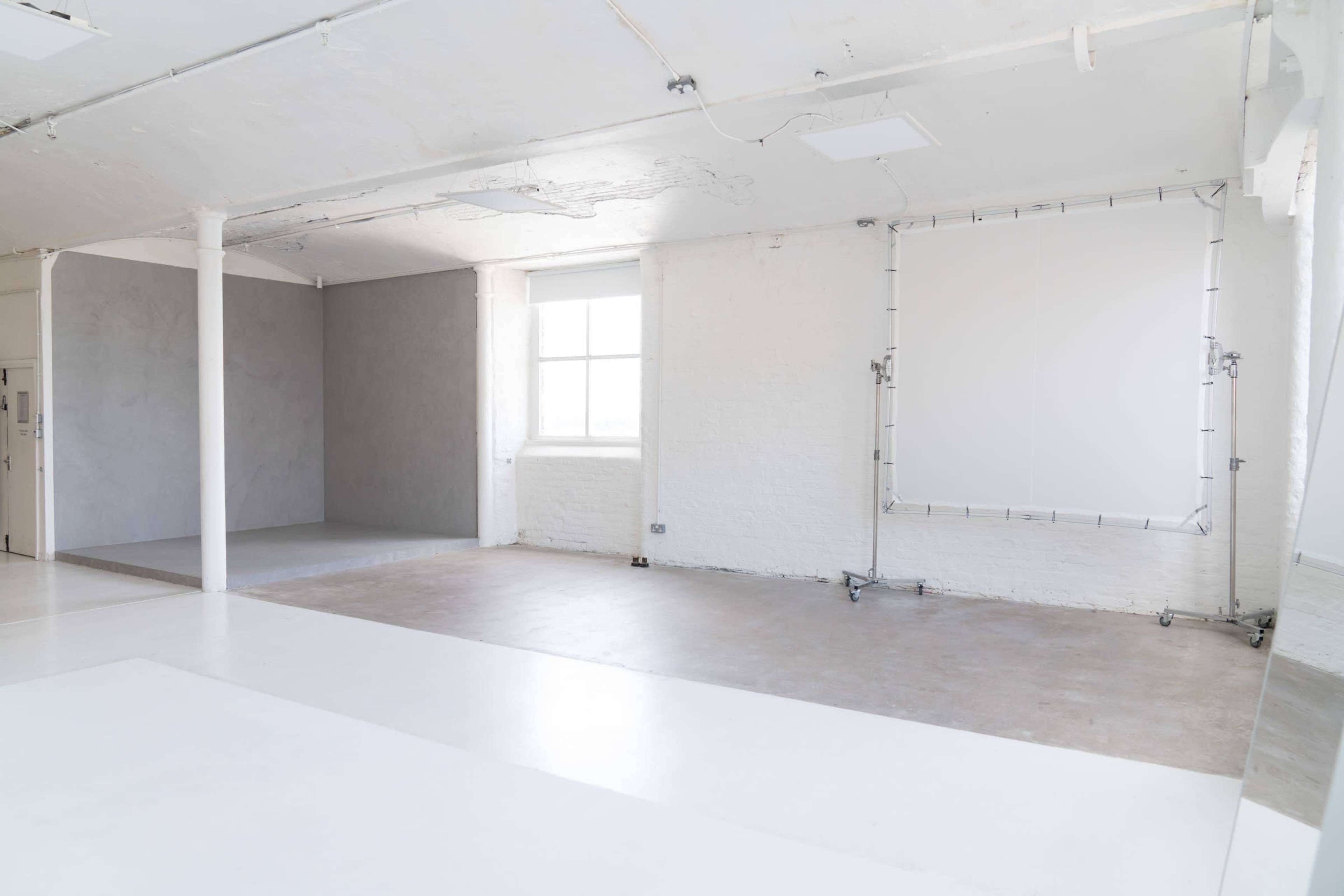 A spacious, empty room with white walls, a window, and a gray area in one corner.