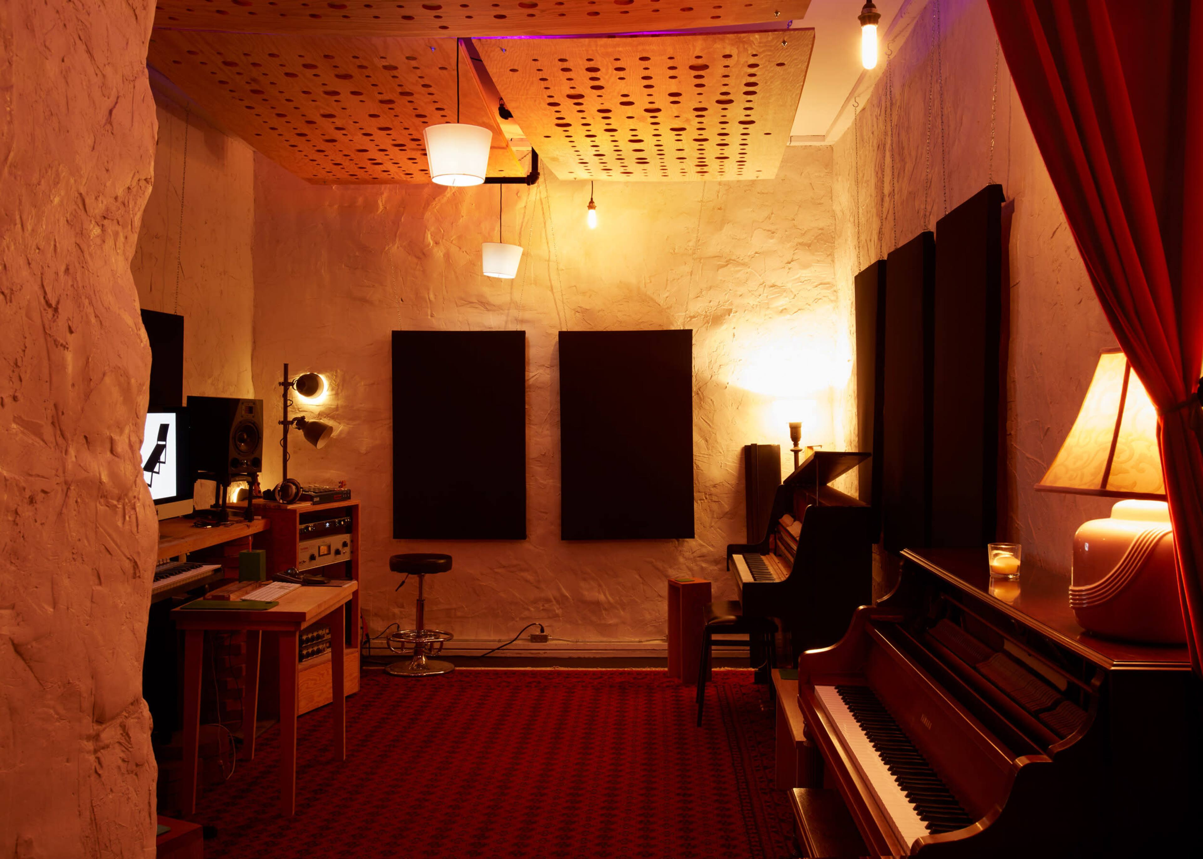 A cozy music studio with a piano, soundproof panels on the walls, and various audio equipment, all illuminated by warm lighting.