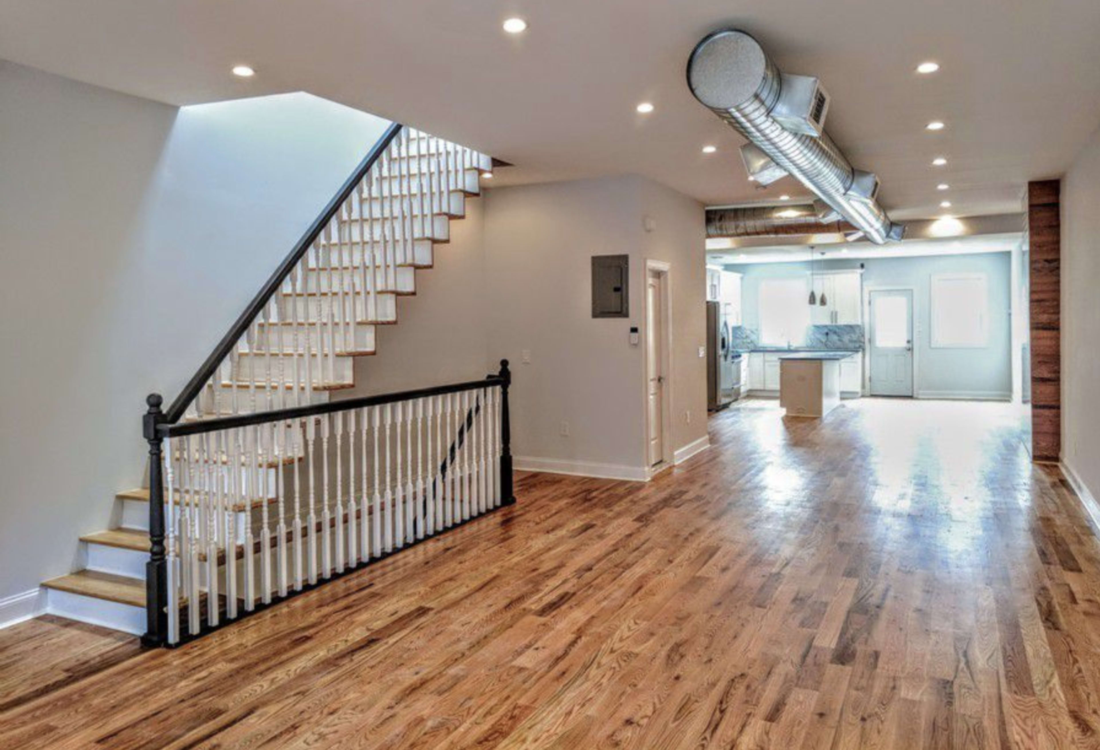 A spacious, modern interior of a home featuring a staircase, hardwood flooring, and an open layout that connects the living area to the kitchen.