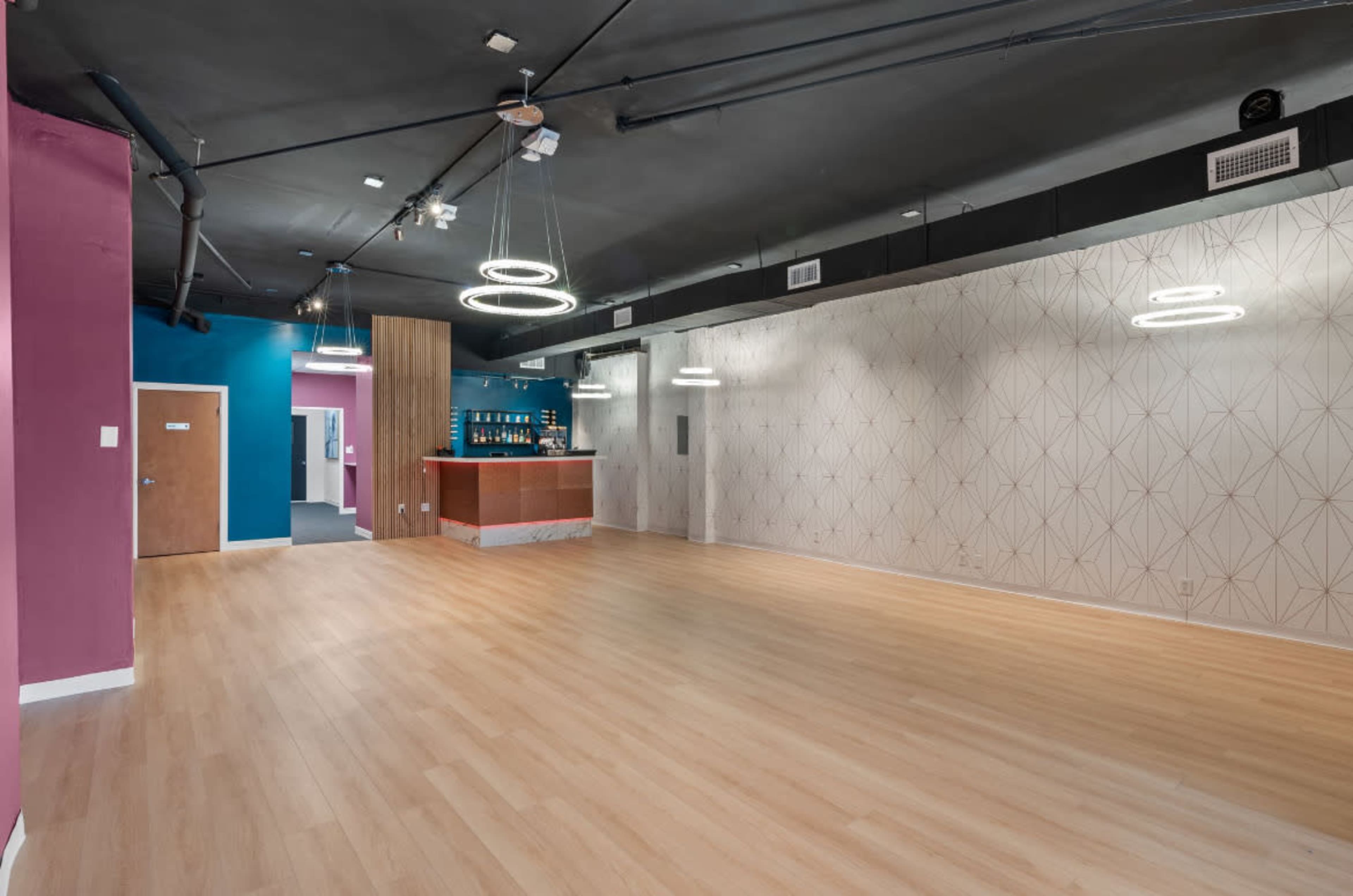 The image shows an empty indoor space with wooden flooring, colorful walls, and modern light fixtures.