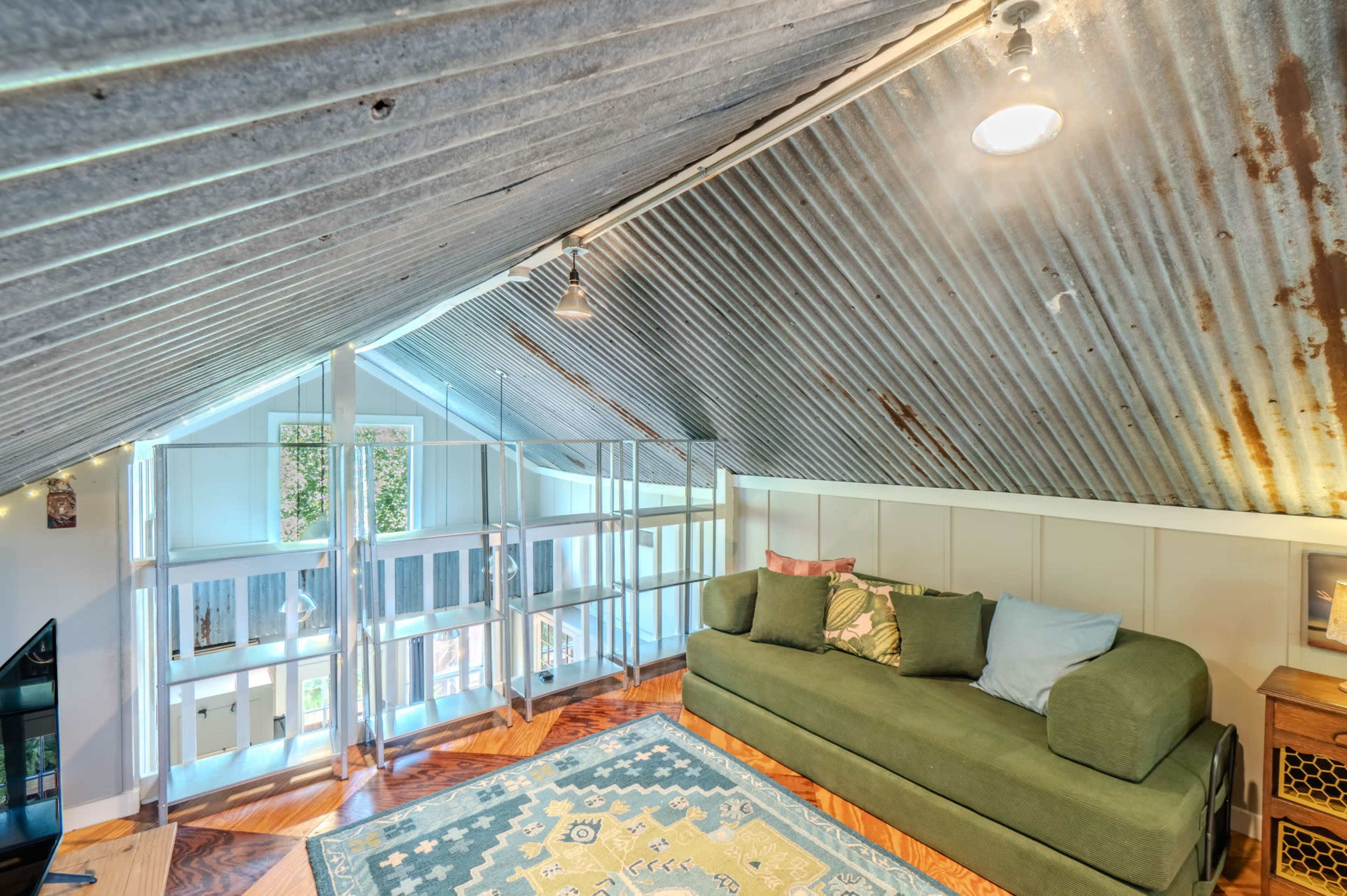 The image shows an attic space with a corrugated metal ceiling, featuring a green sofa and a patterned area rug.