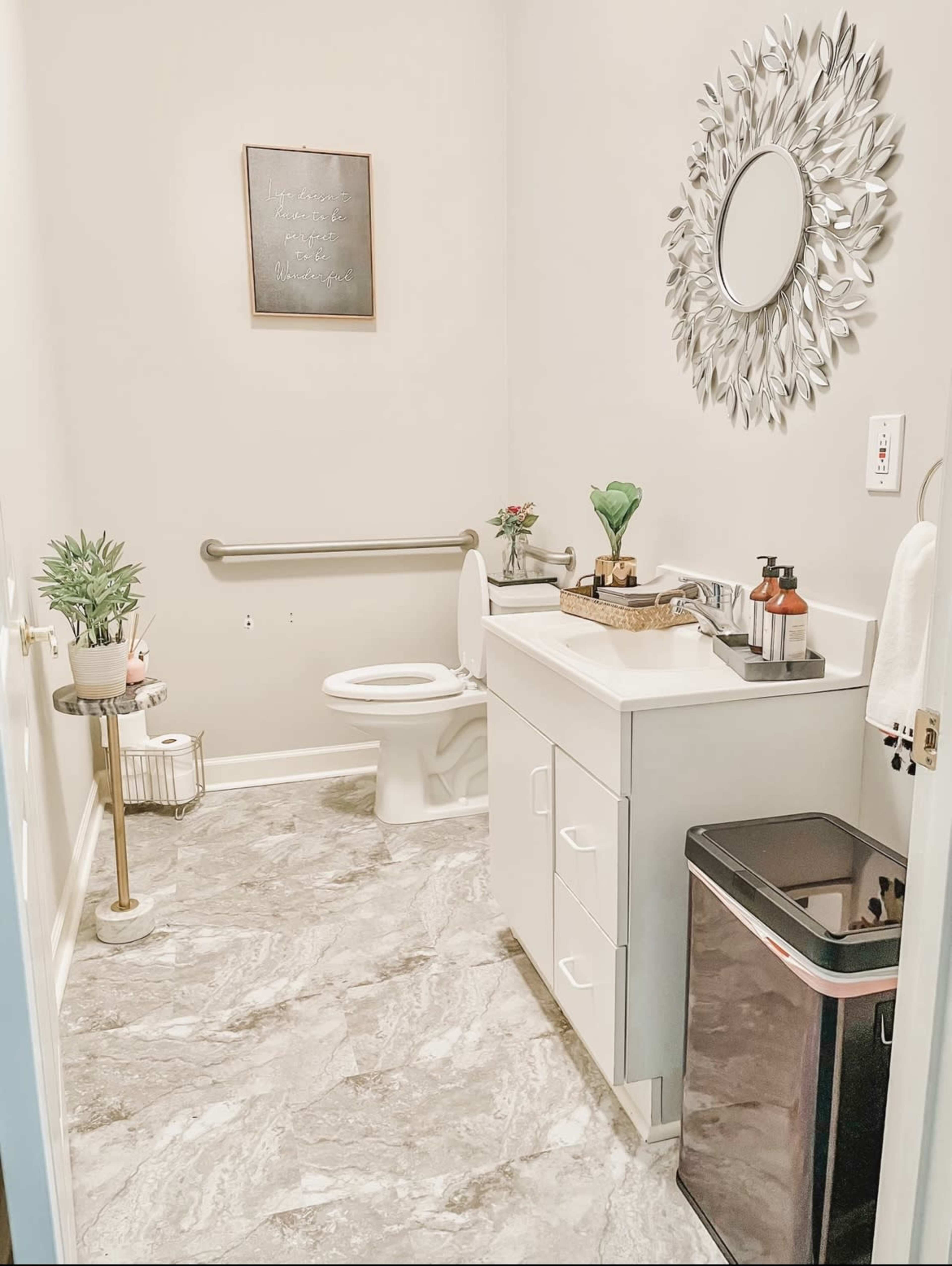 A clean bathroom featuring a toilet, a sink with modern fixtures, a large mirror, and decorative plants on the countertop.