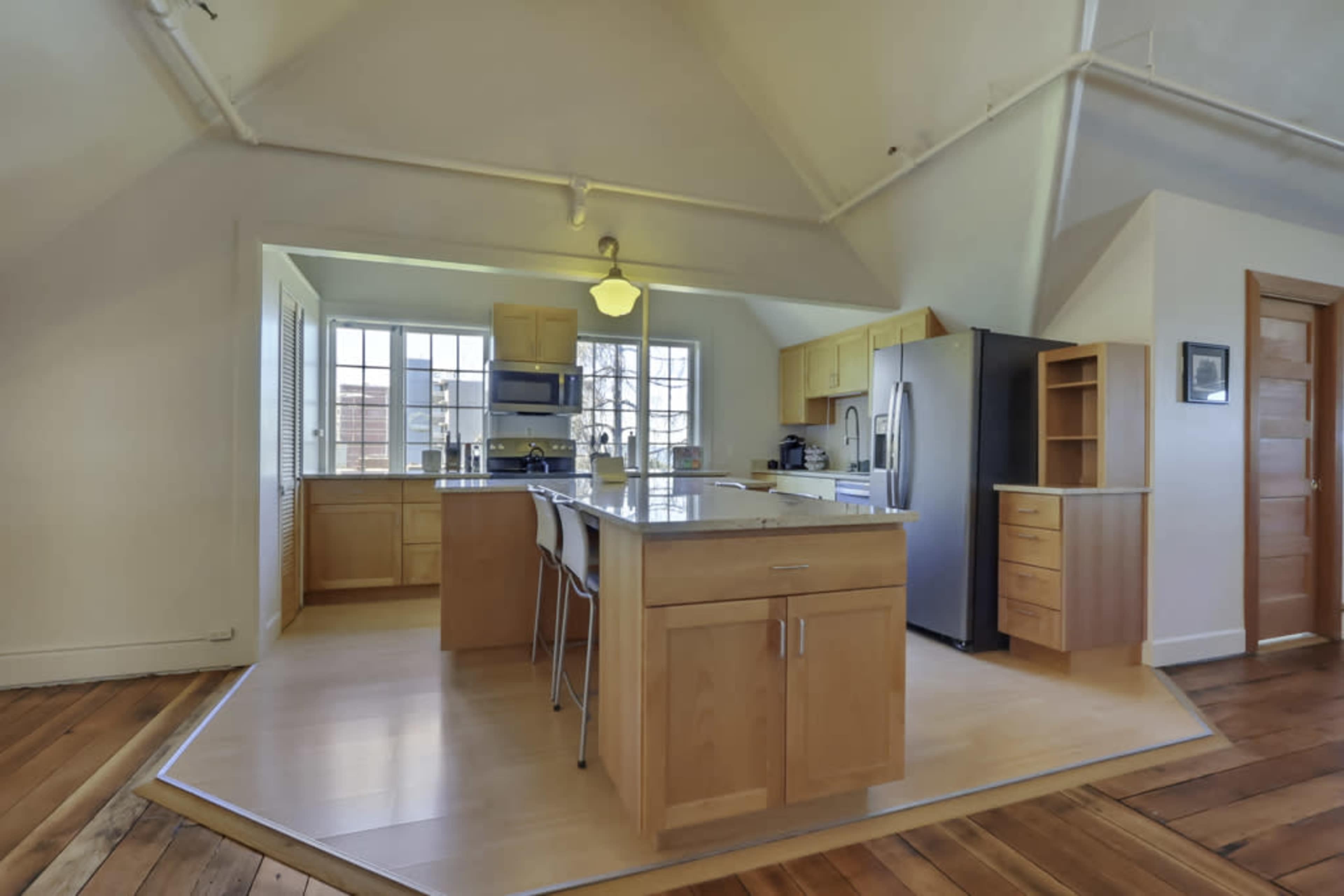A modern kitchen with wooden cabinets, a central island with seating, and stainless steel appliances.