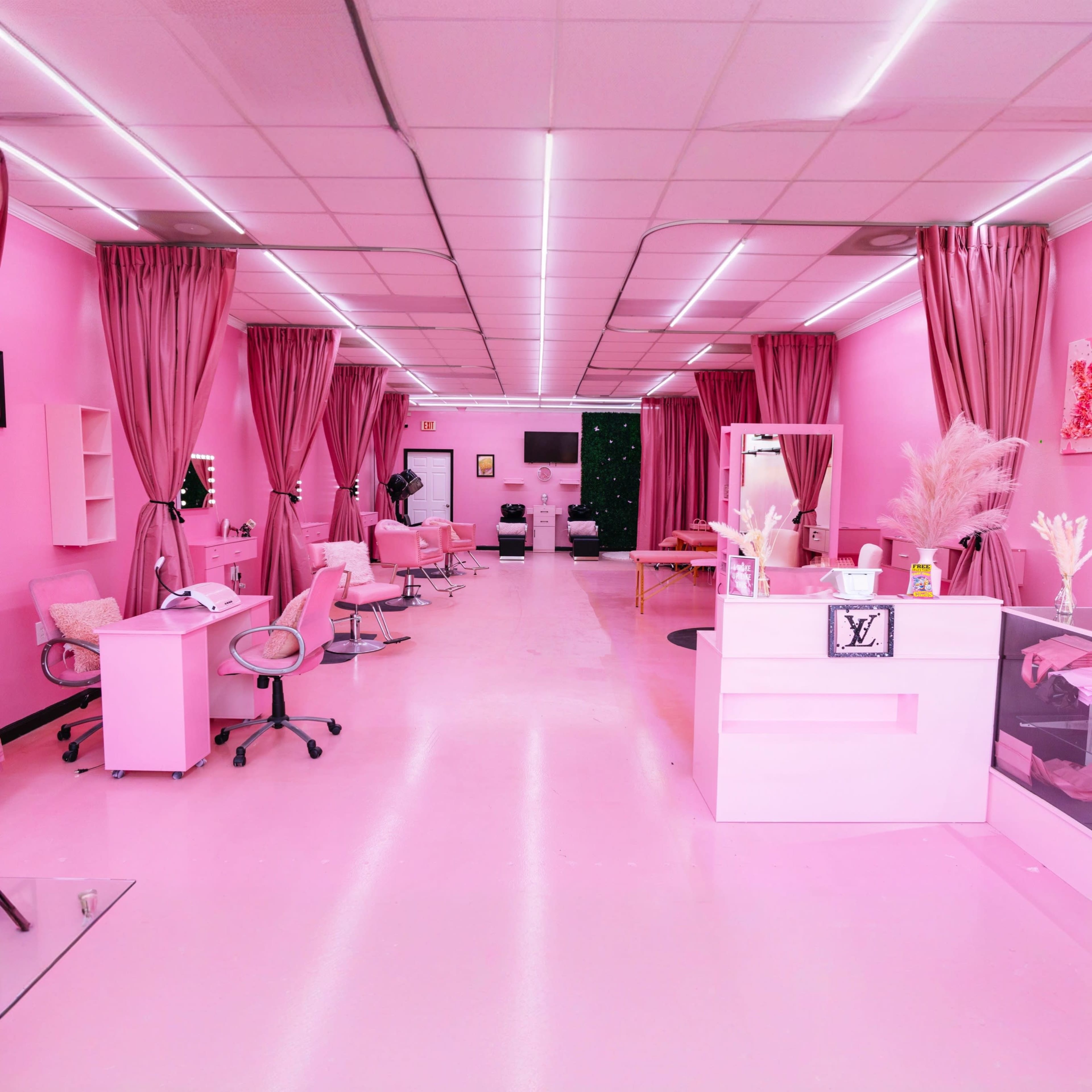 A brightly lit salon interior features pink walls, chairs, and curtains, with elegant decor and a reception area displaying a Louis Vuitton logo.