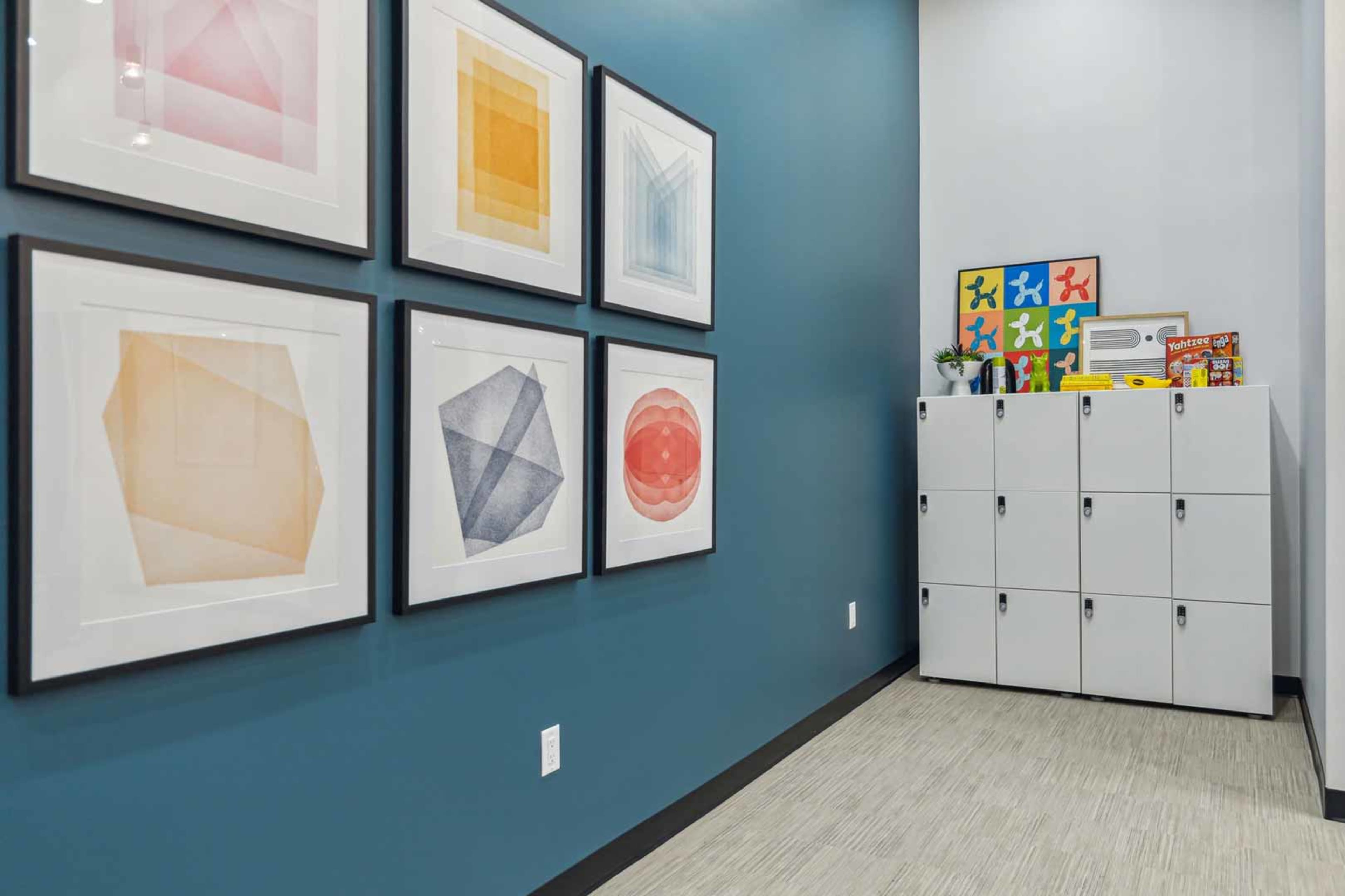 A corner of a room with framed geometric art hanging on a blue wall next to a row of white lockers.