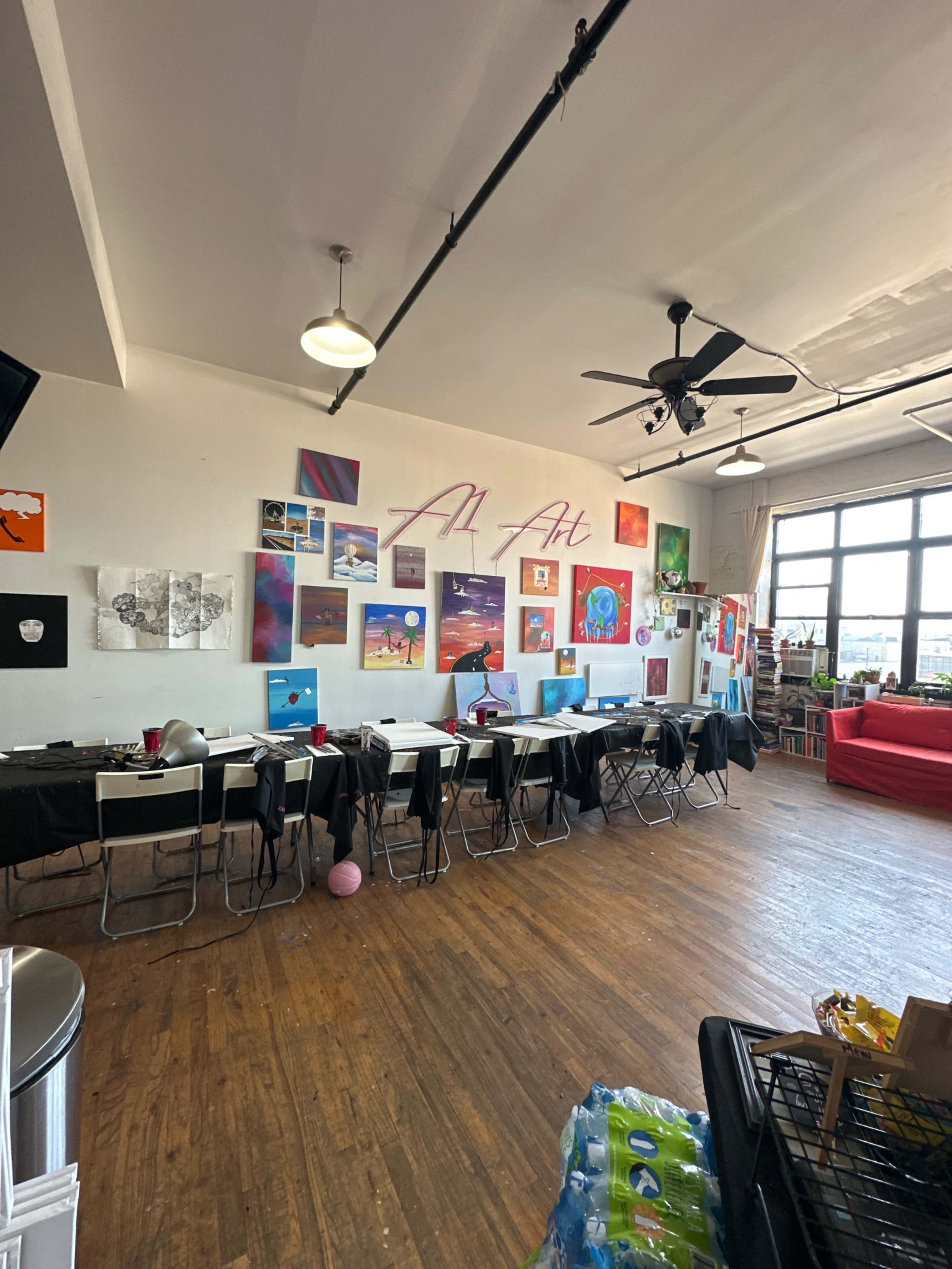 A spacious room with tables set up for an event, decorated with various artworks on the walls and large windows letting in natural light.