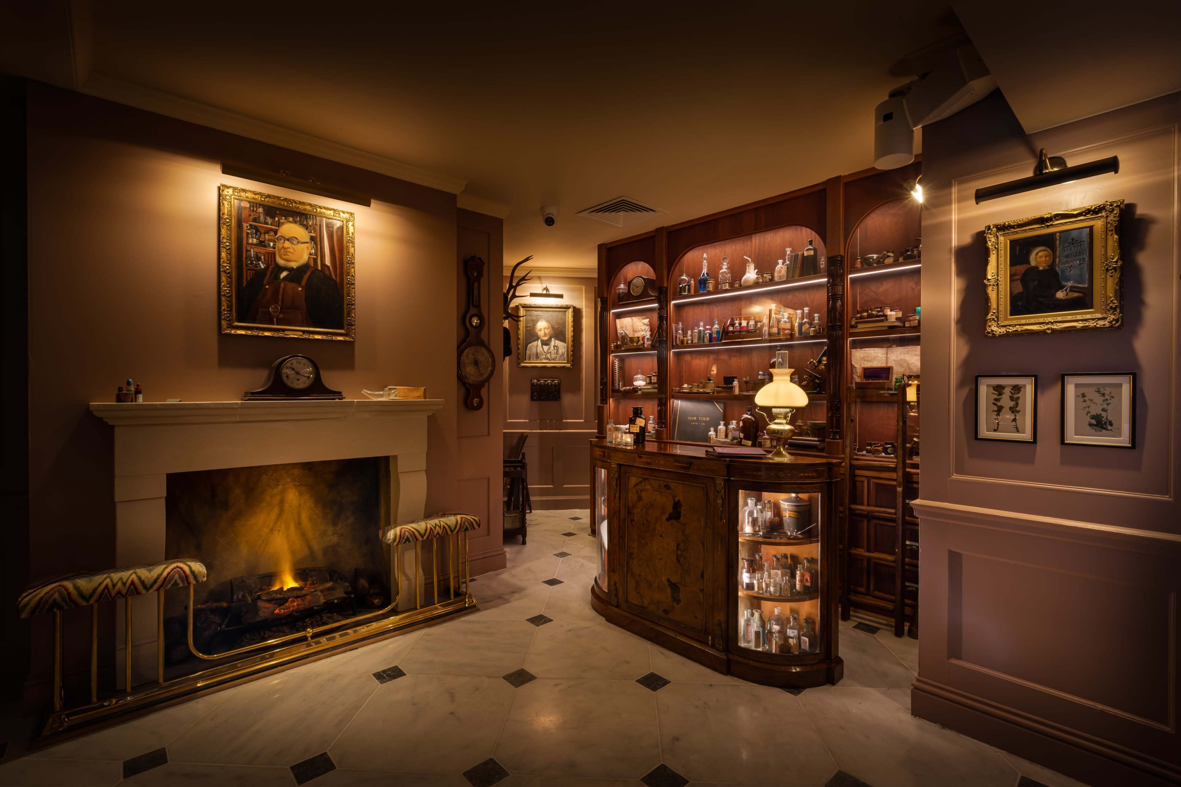 A warmly lit room with a fireplace, a vintage bar filled with bottles, and portraits hanging on the walls.