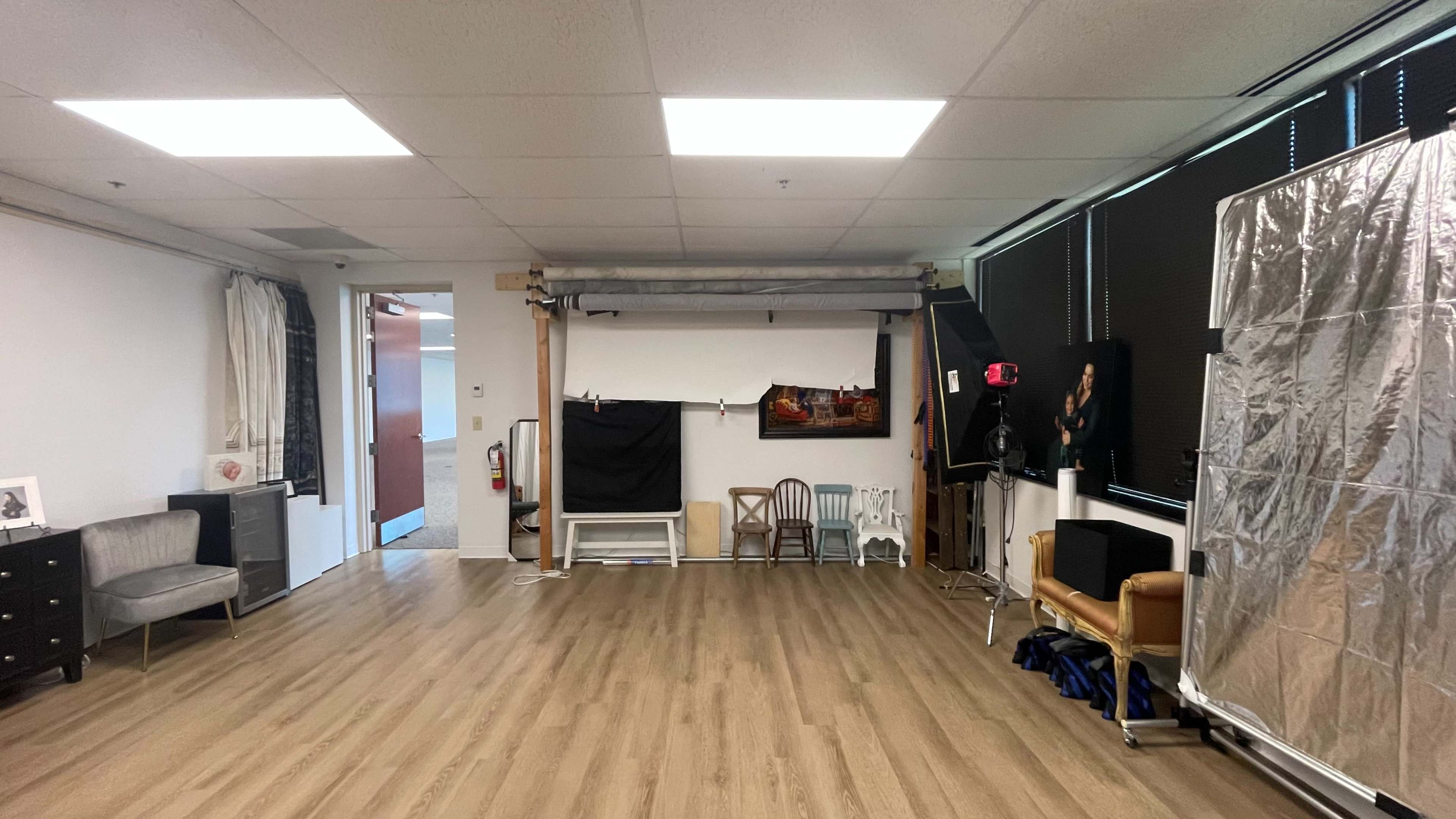 The image shows a spacious room equipped with photography backdrops, lighting equipment, and a mix of furniture including a chair, a table, and a cabinet.