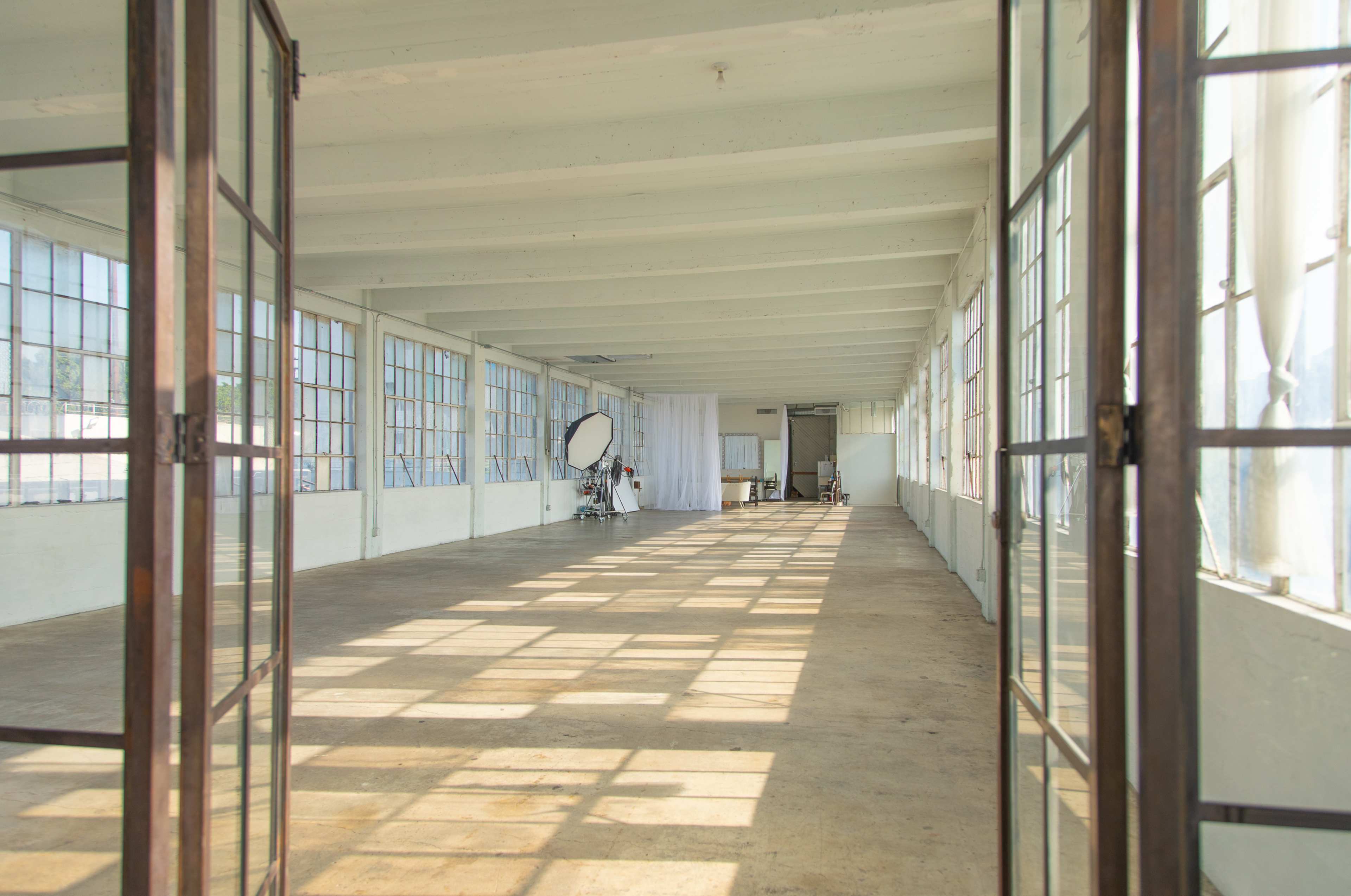 A large, empty warehouse space with multiple windows allowing natural light to fill the room.