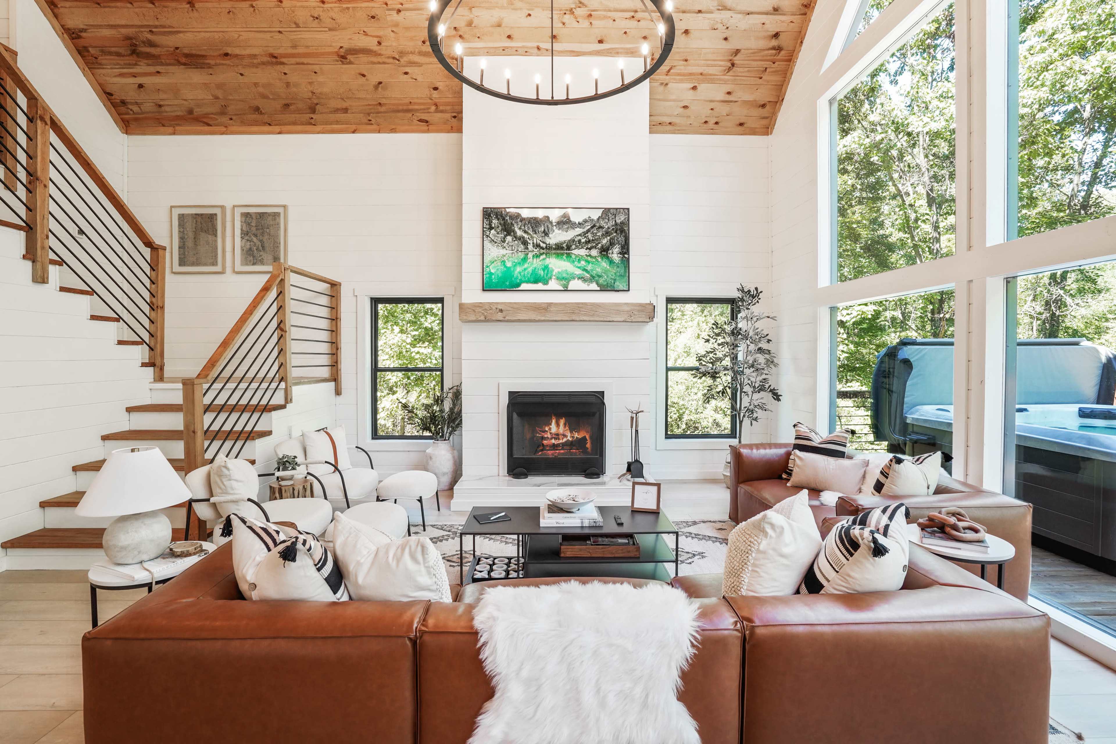 A spacious living room features a brown leather sectional, a central coffee table, and a modern fireplace, with large windows allowing natural light to fill the space.
