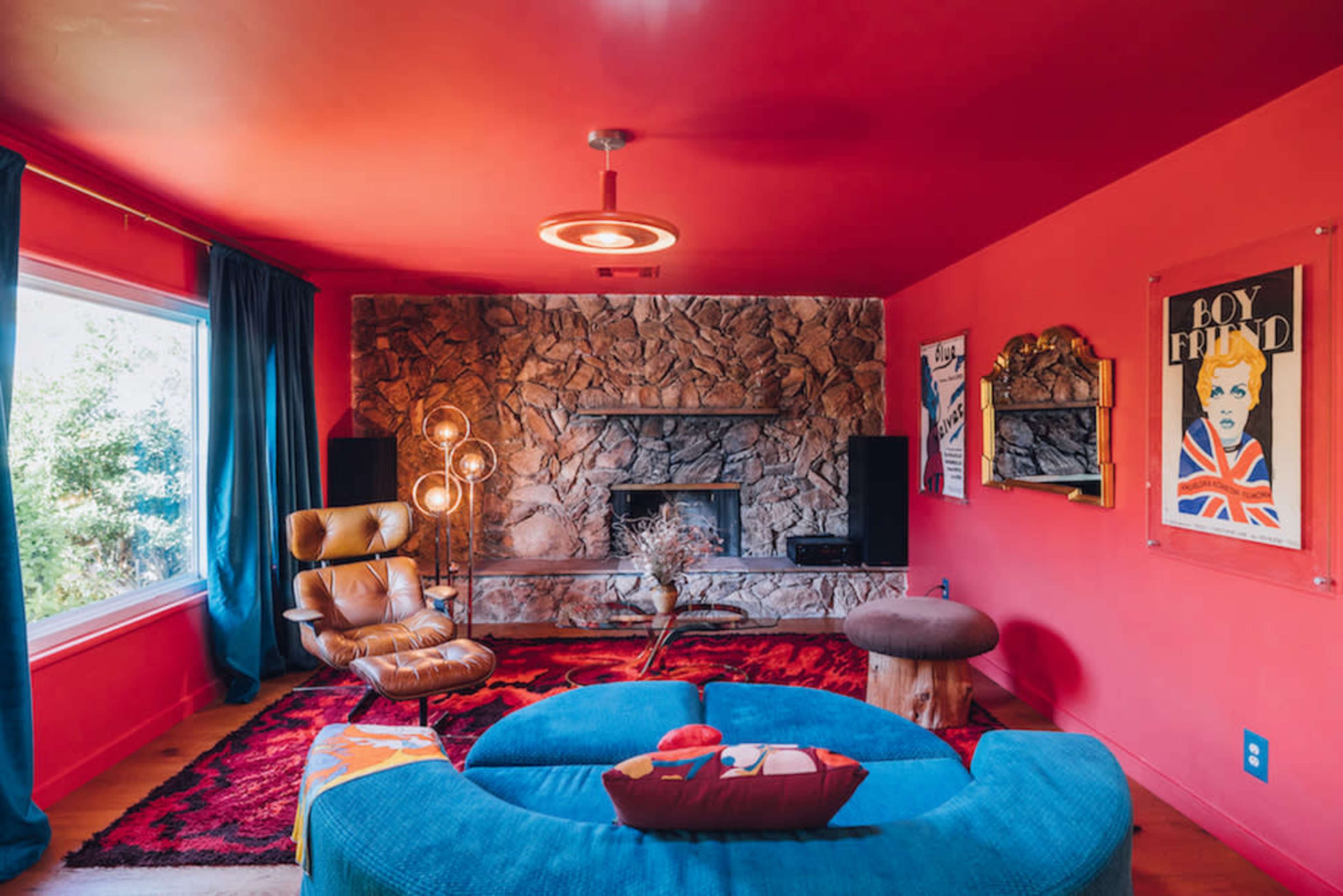 The living room features a bright red wall, a stone fireplace, and a curved blue sofa arranged around a decorative rug.