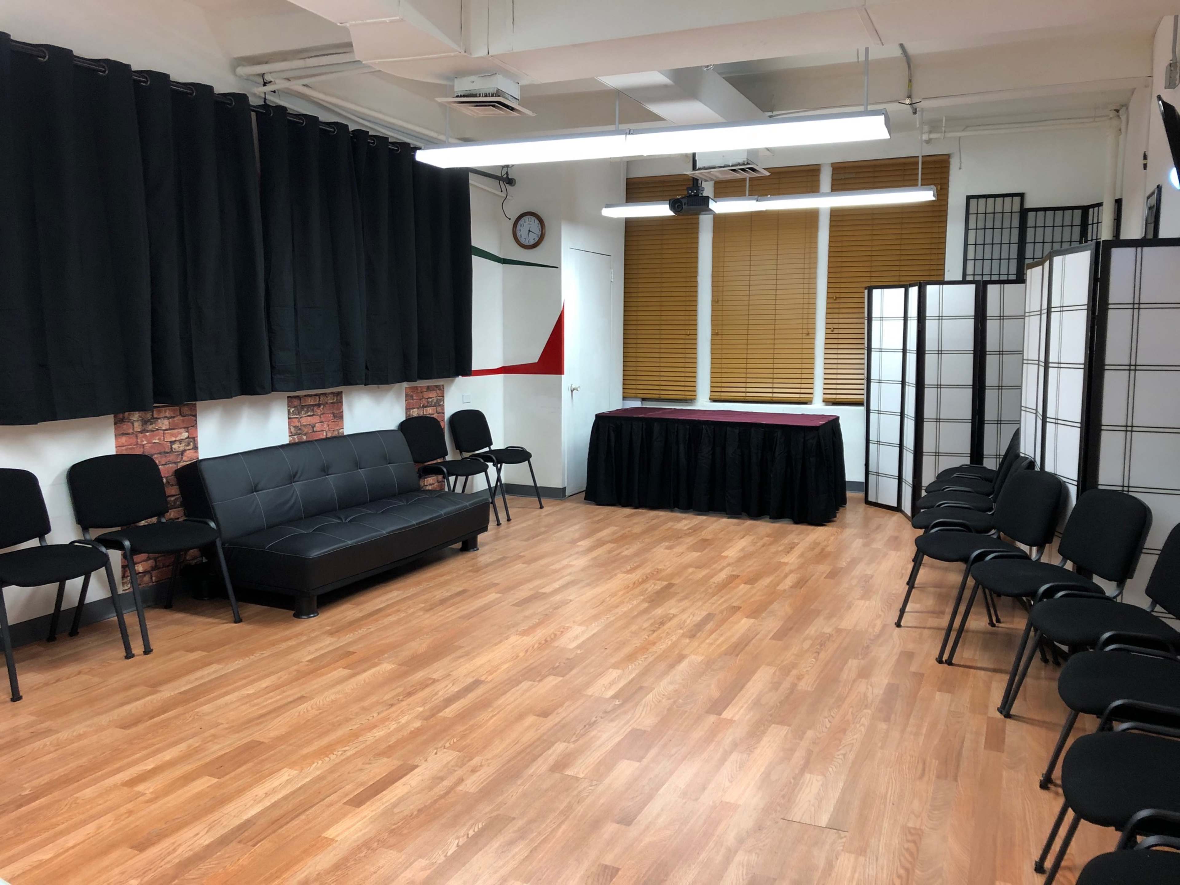 An empty room features a black sofa, several chairs arranged around the space, and a table draped in black fabric at the front.