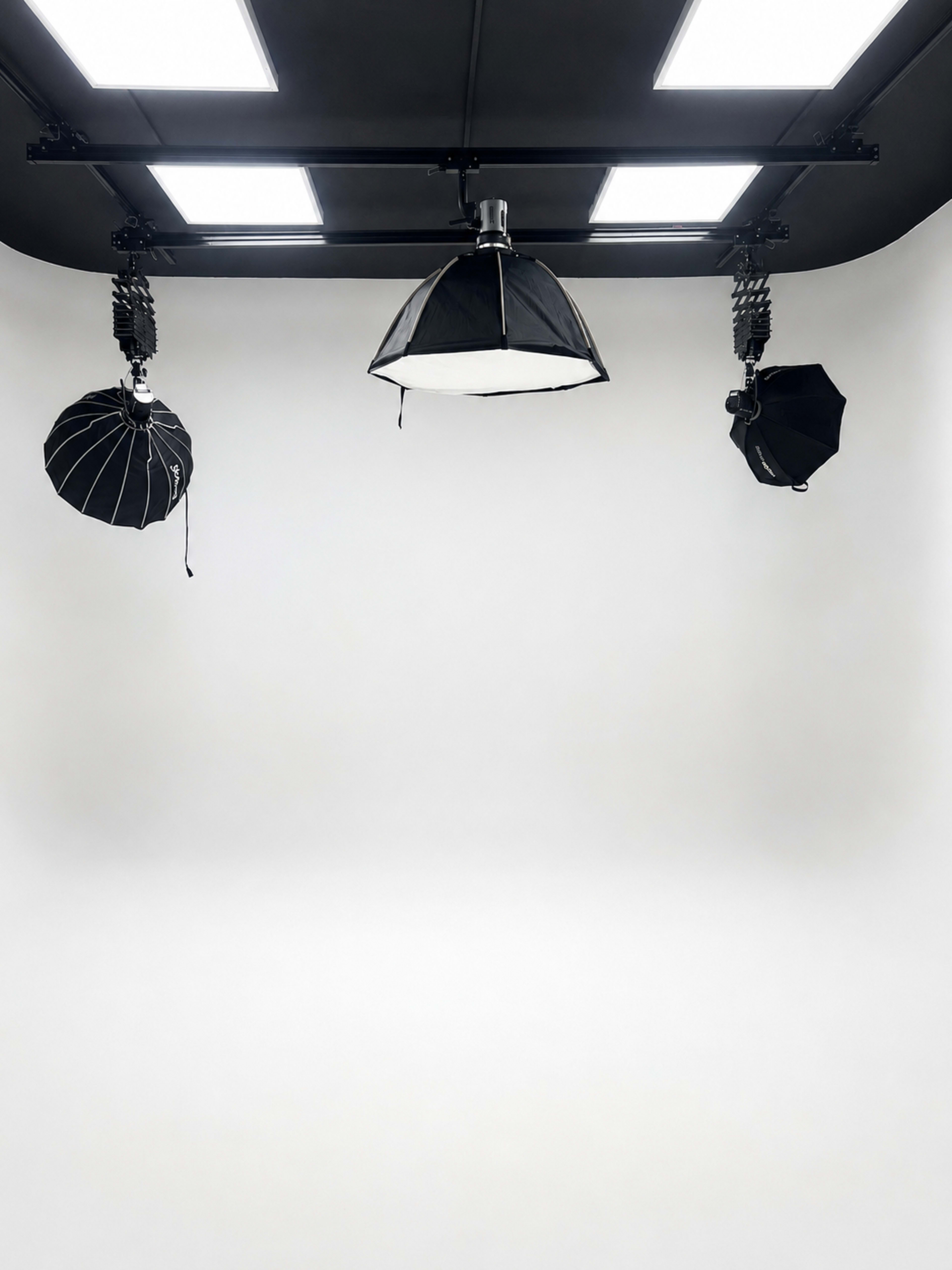 The image shows a minimal studio setup with three different light modifiers suspended from a rail against a blank white backdrop.