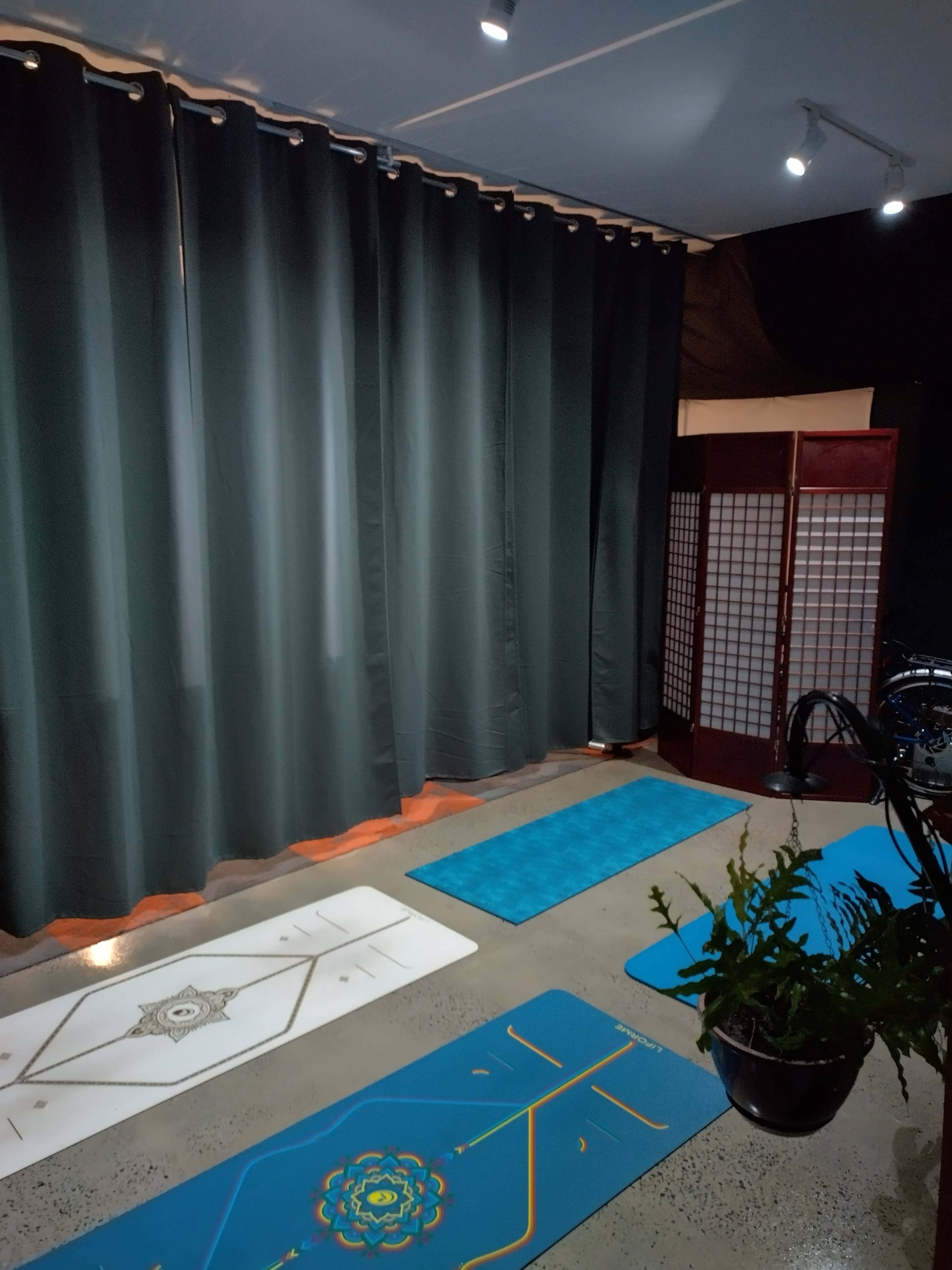A quiet room with yoga mats placed on a concrete floor, surrounded by dark curtains and a decorative screen in the background.