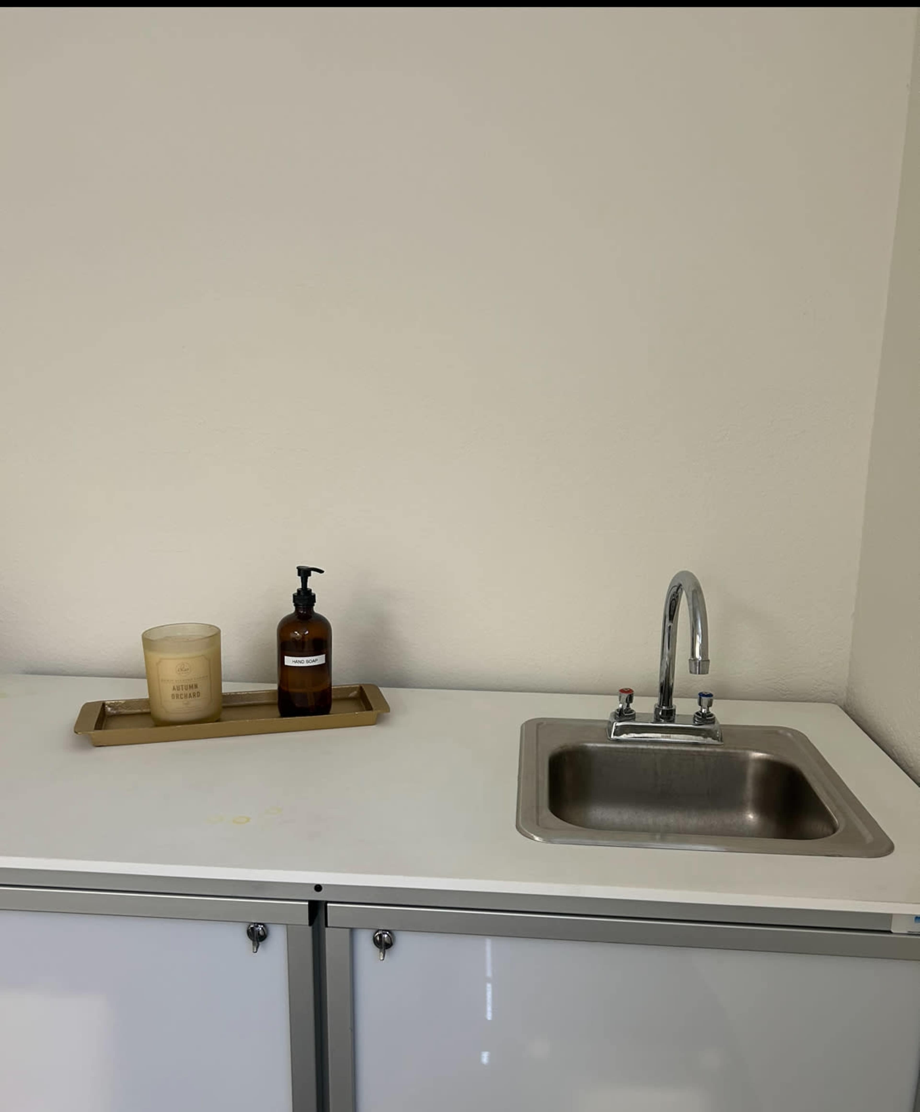 A countertop with a small sink, a soap dispenser, and a candle on a wooden tray.