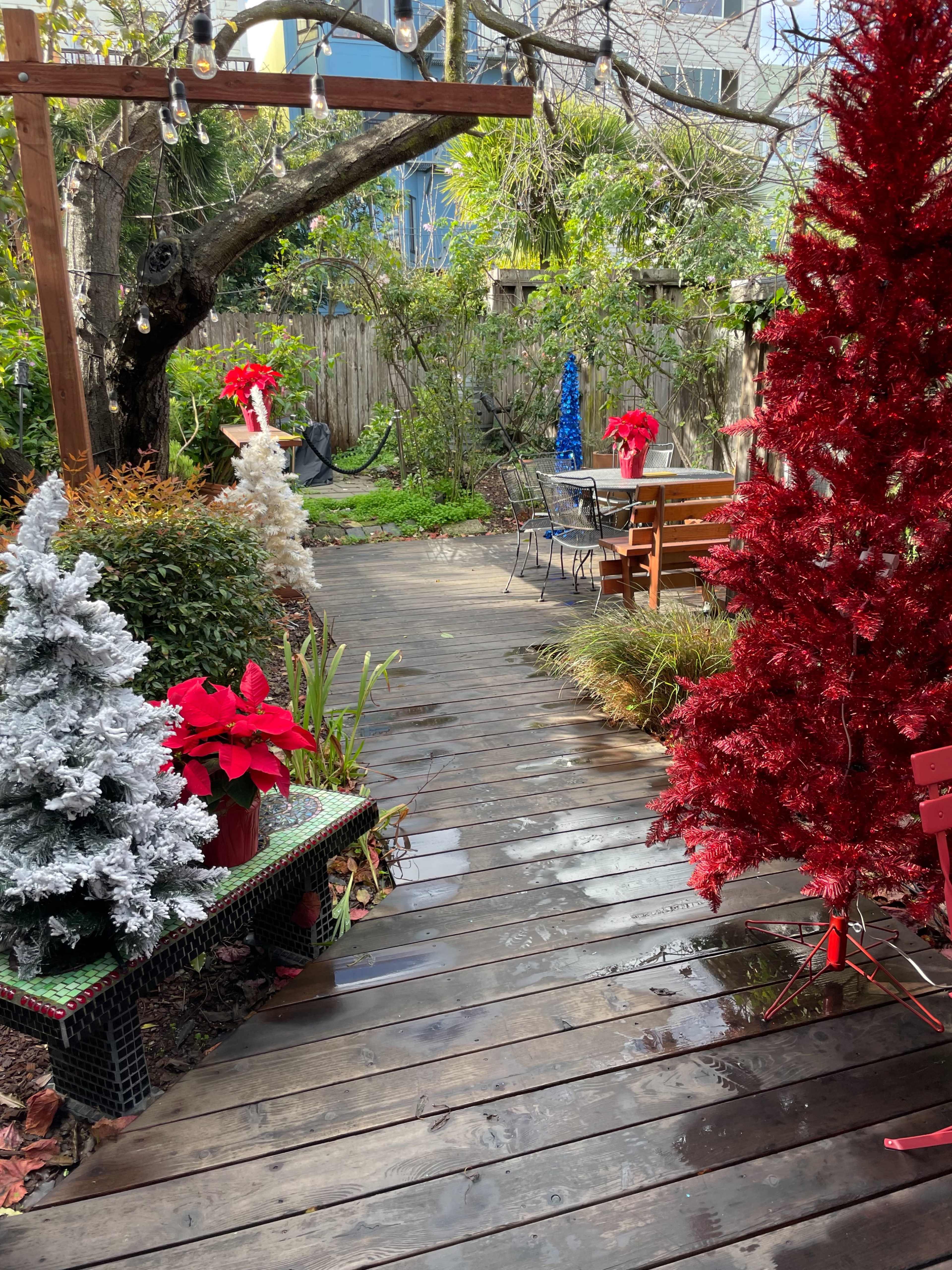 A wooden pathway leads through a festive garden decorated with red and white Christmas trees and potted poinsettias.
