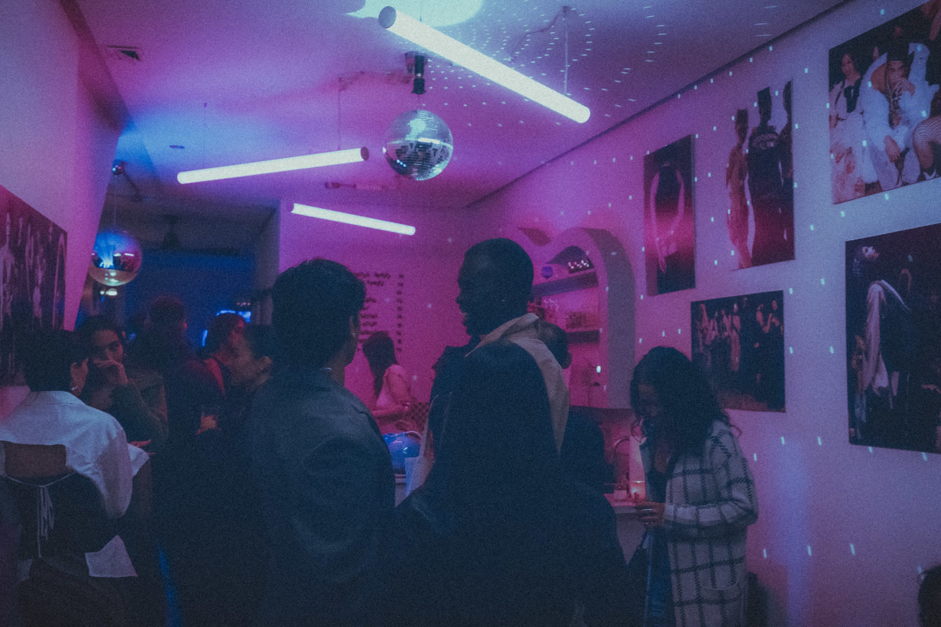 People are socializing in a dimly lit venue with colorful lighting and decorative disco balls hanging from the ceiling.