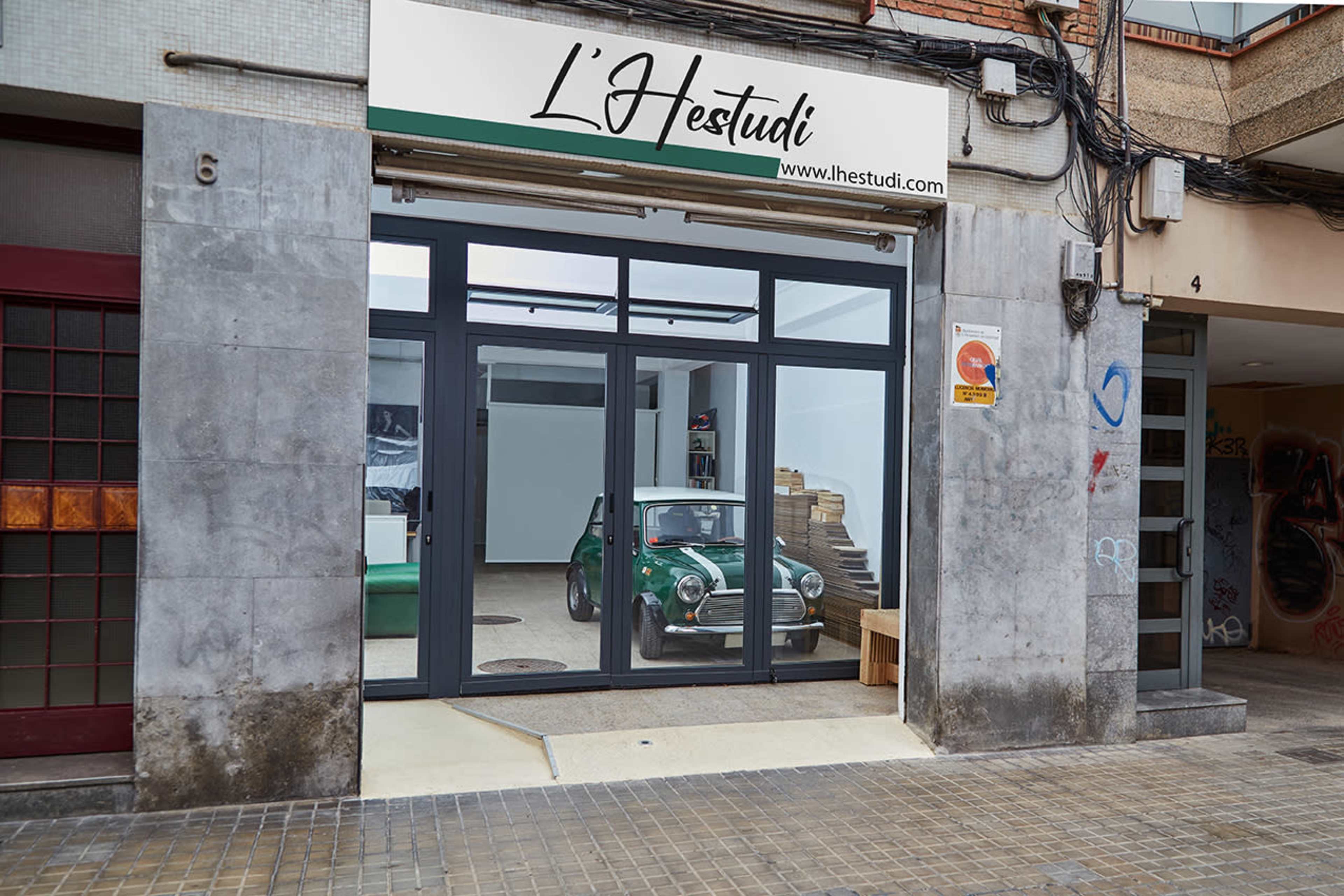 The image shows a storefront with glass doors displaying a green car inside an art studio.