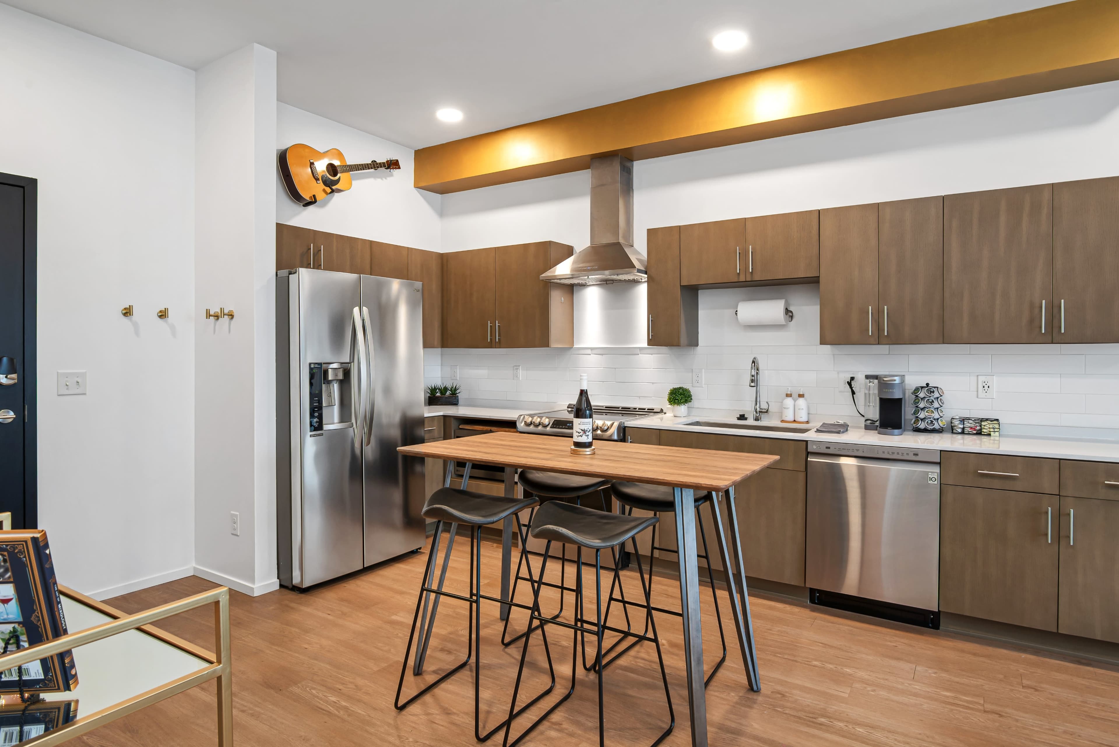 A modern kitchen features stainless steel appliances, wooden cabinetry, and a dining area with high stools.