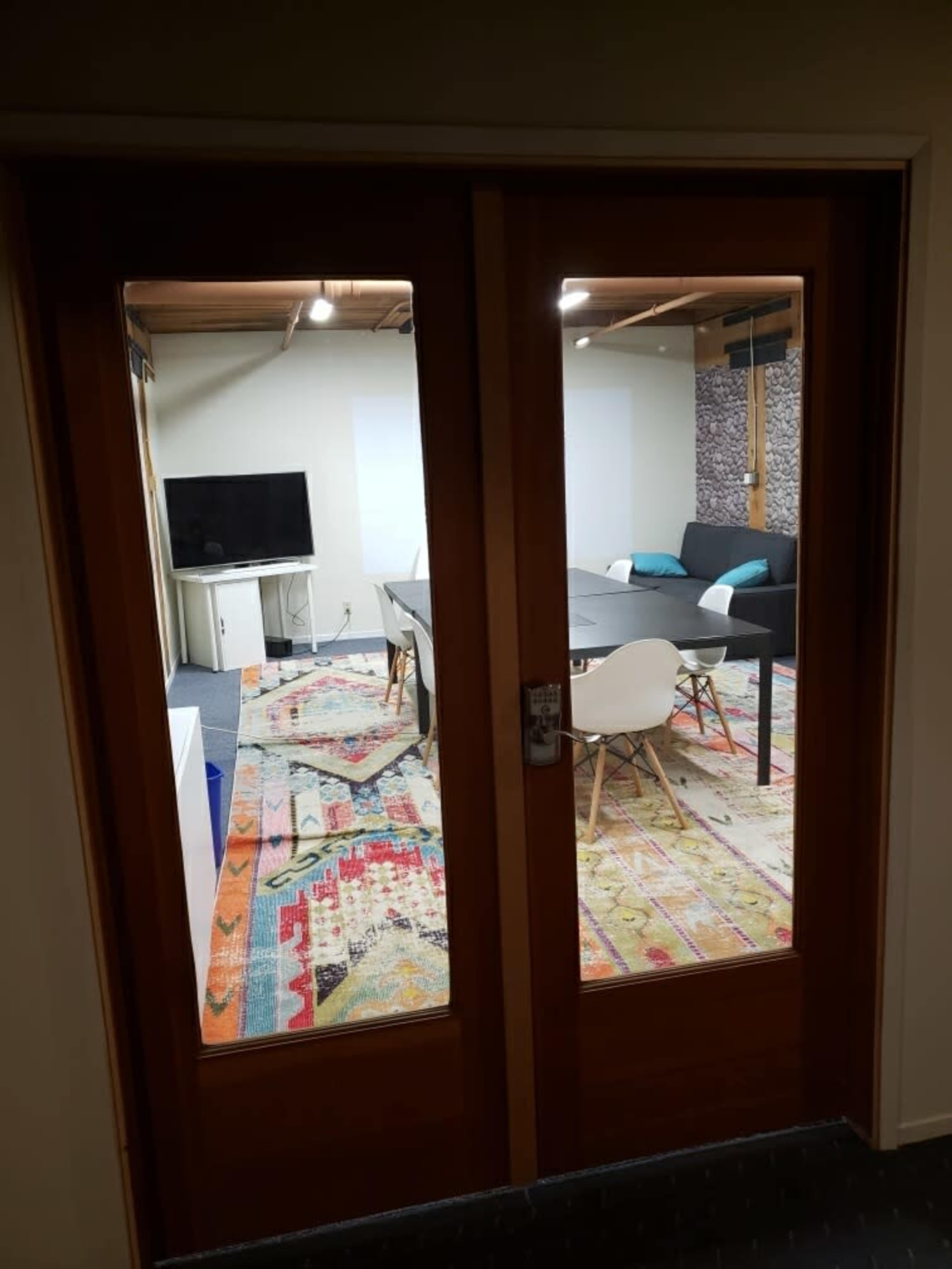 A room with a wooden door, leading into a space that features a large table, chairs, a television, and a colorful area rug.