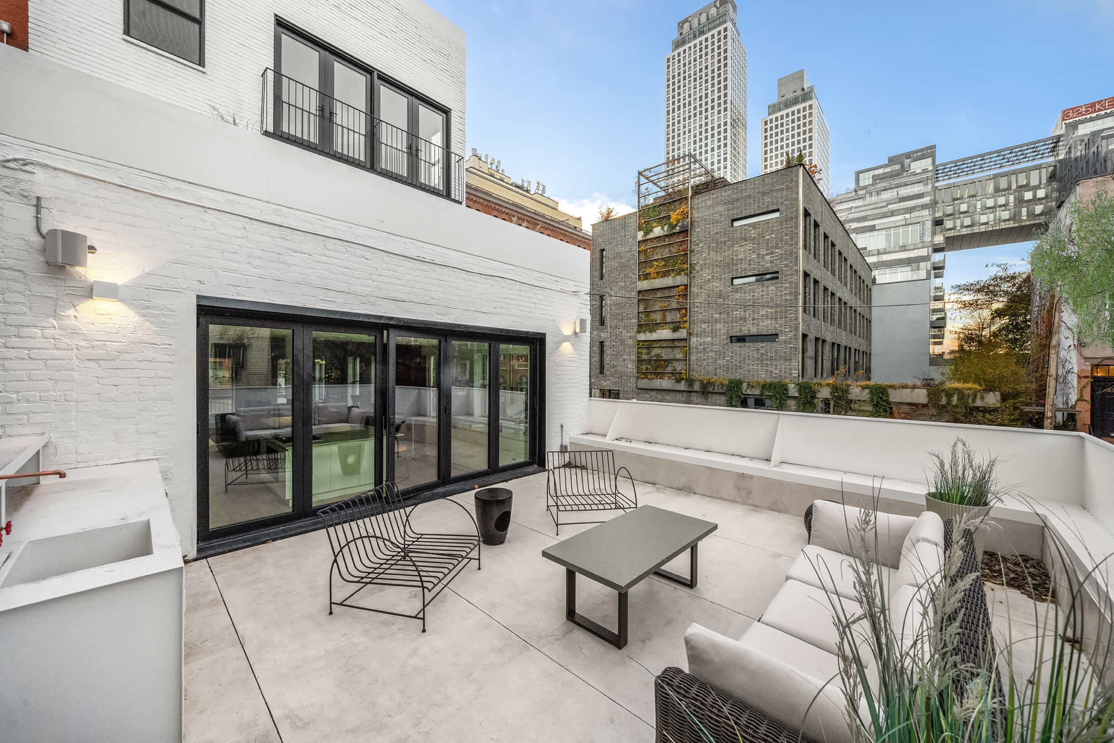 The image shows a modern outdoor patio area featuring a seating arrangement, a table, and a view of surrounding buildings in an urban environment.