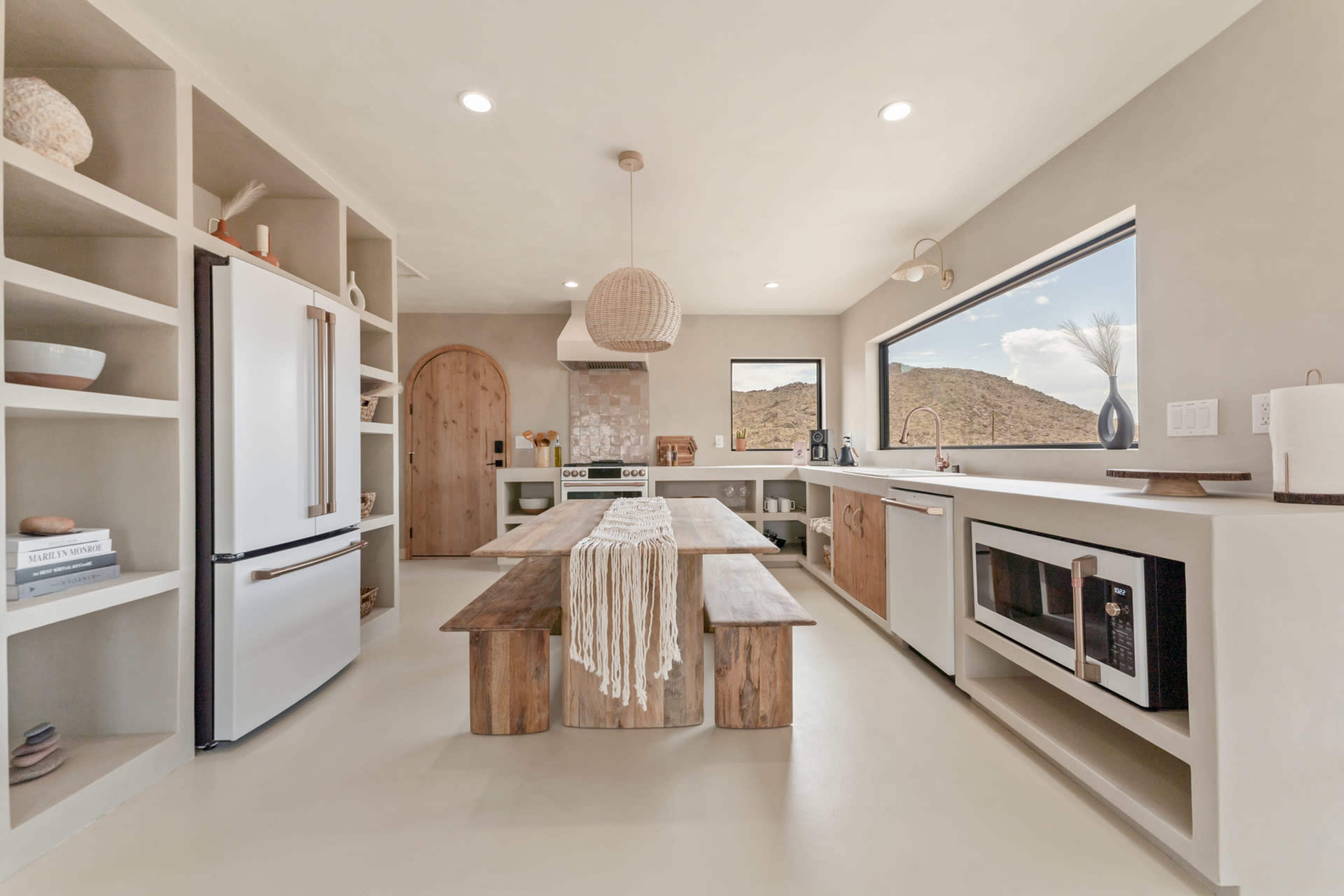 A modern kitchen with a large wooden table, open shelves, and various appliances, including a refrigerator and a microwave.