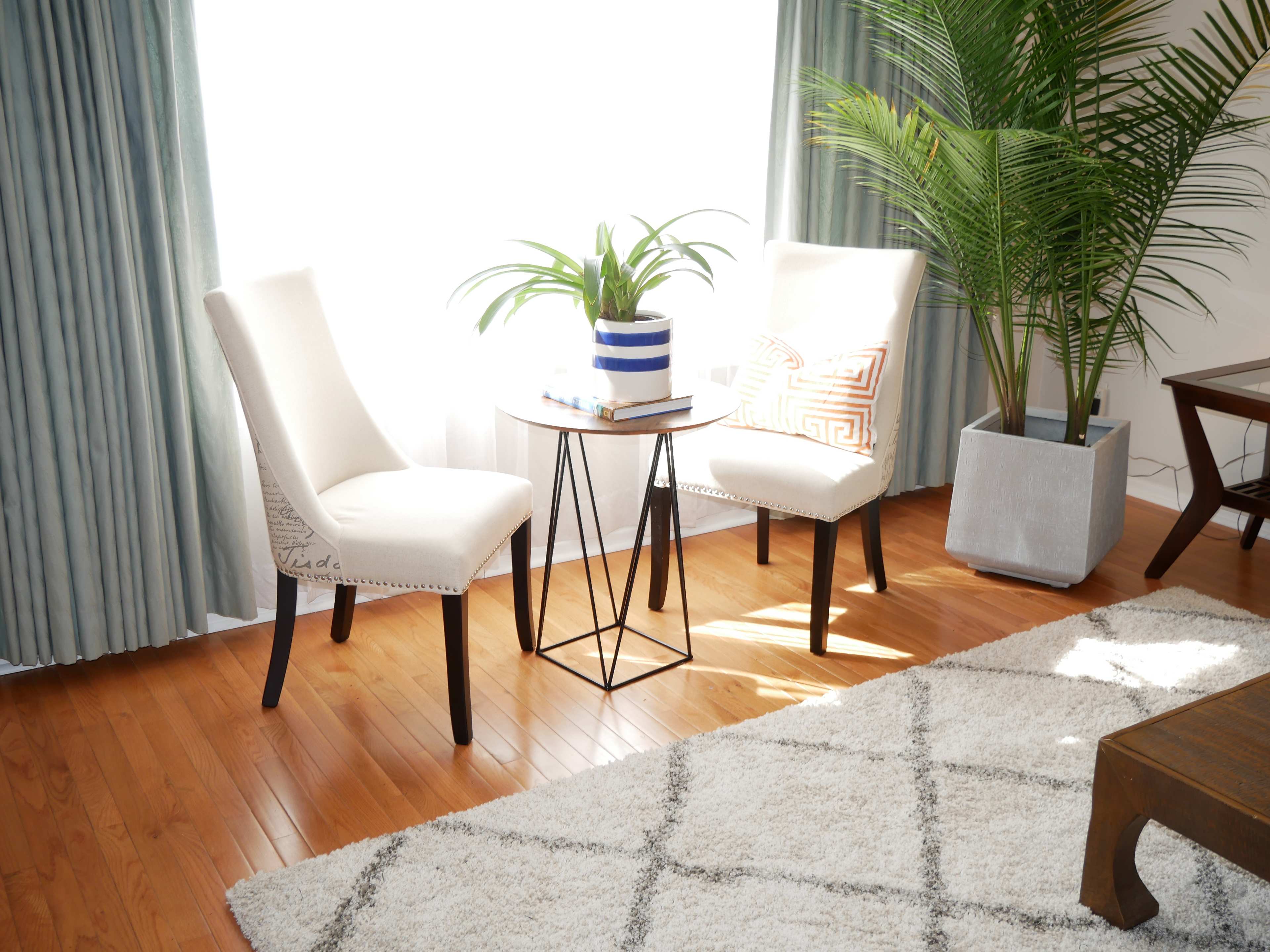 A brightly lit room features two chairs and a small table on a wooden floor, complemented by a plant and patterned decor.