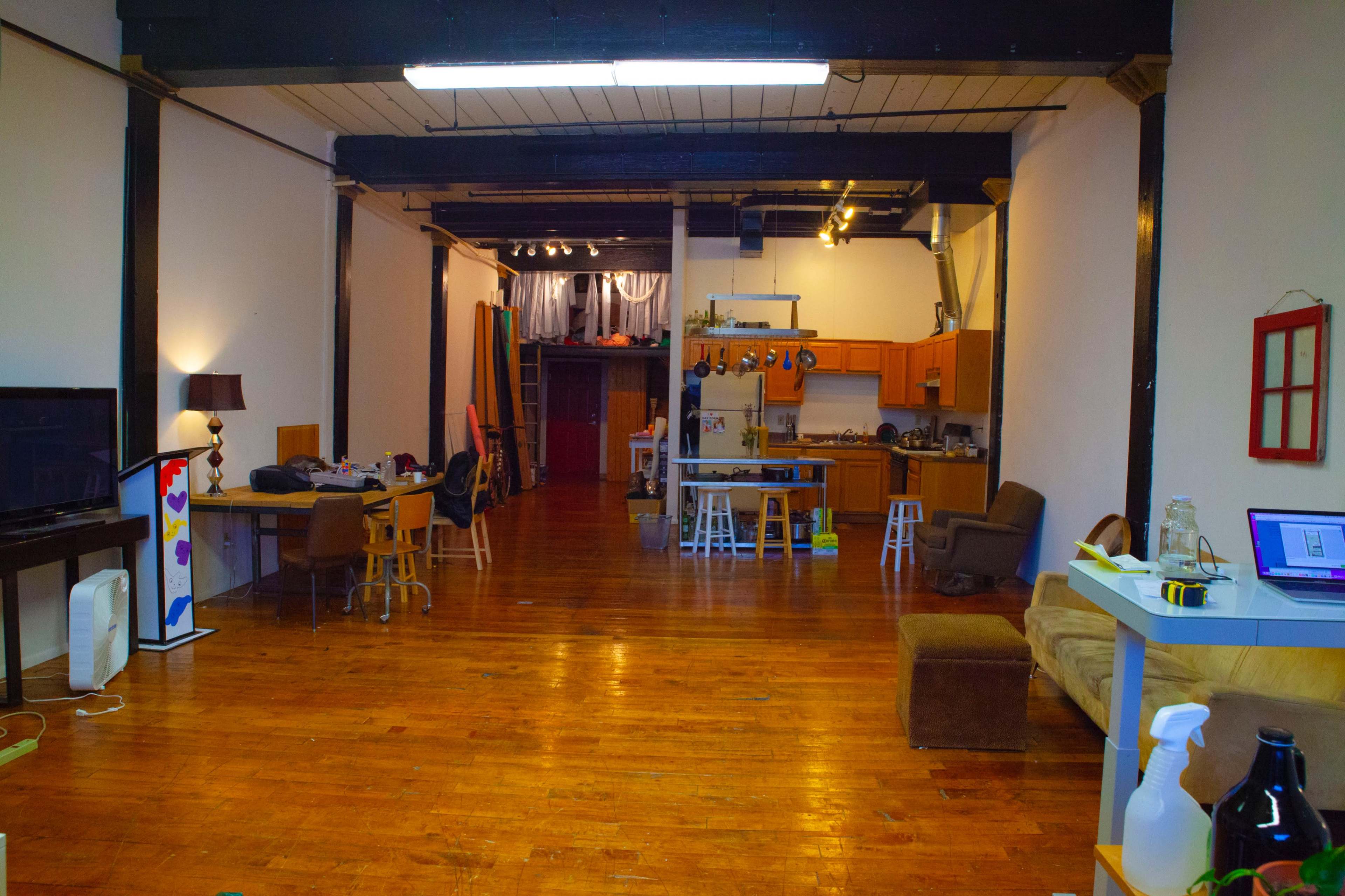 A spacious, open-concept loft with wooden floors, a kitchen area, and various furniture arrangements.