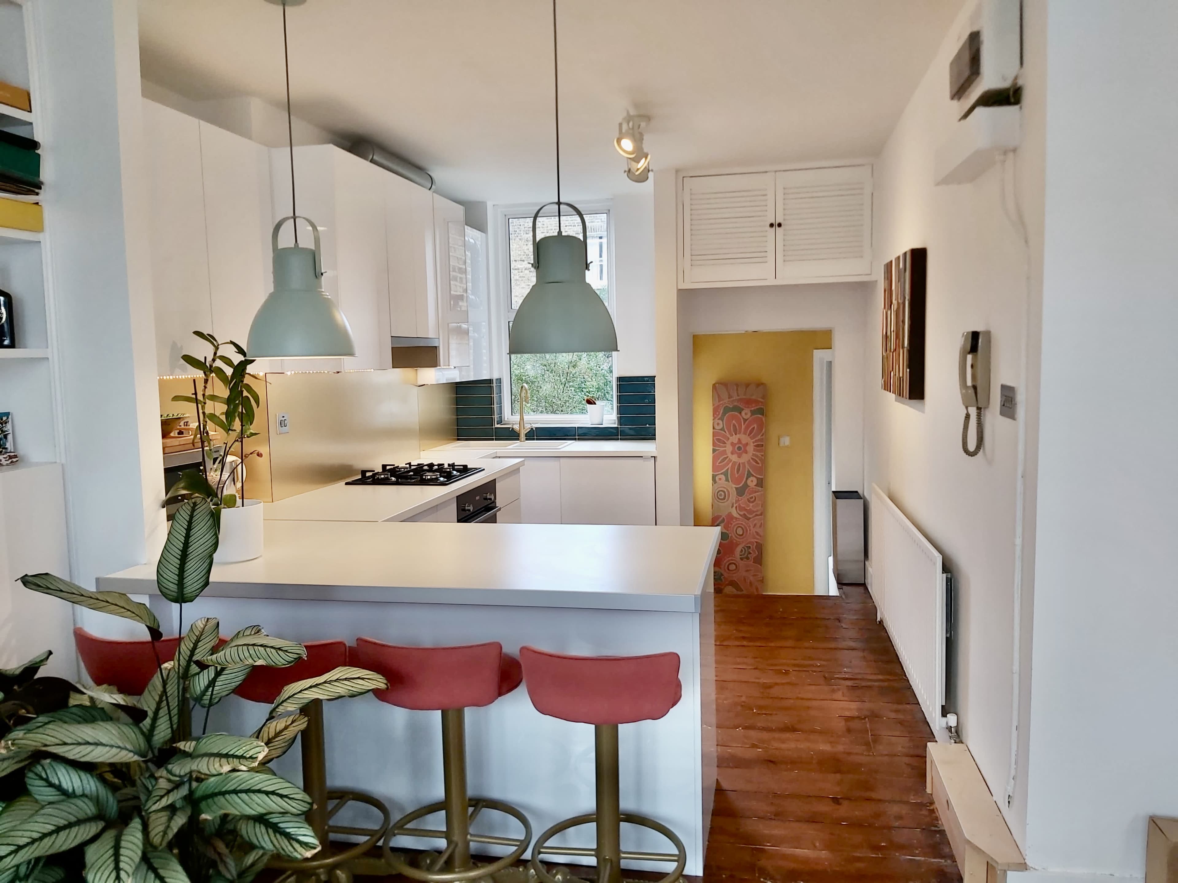 A modern kitchen features white cabinetry, a central island with three pink bar stools, and pendant lighting.