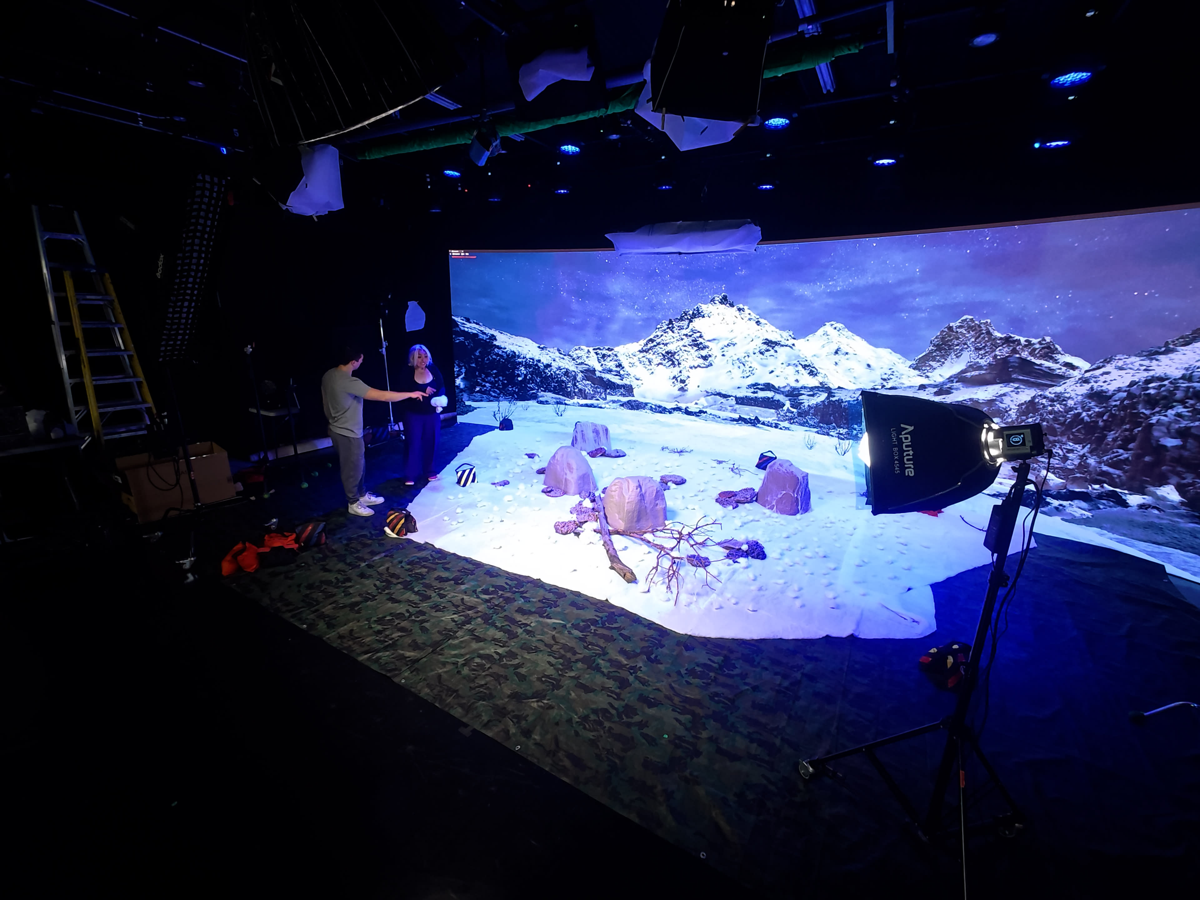 A person is setting up a photography scene featuring a snowy mountain landscape on a large screen in a studio.