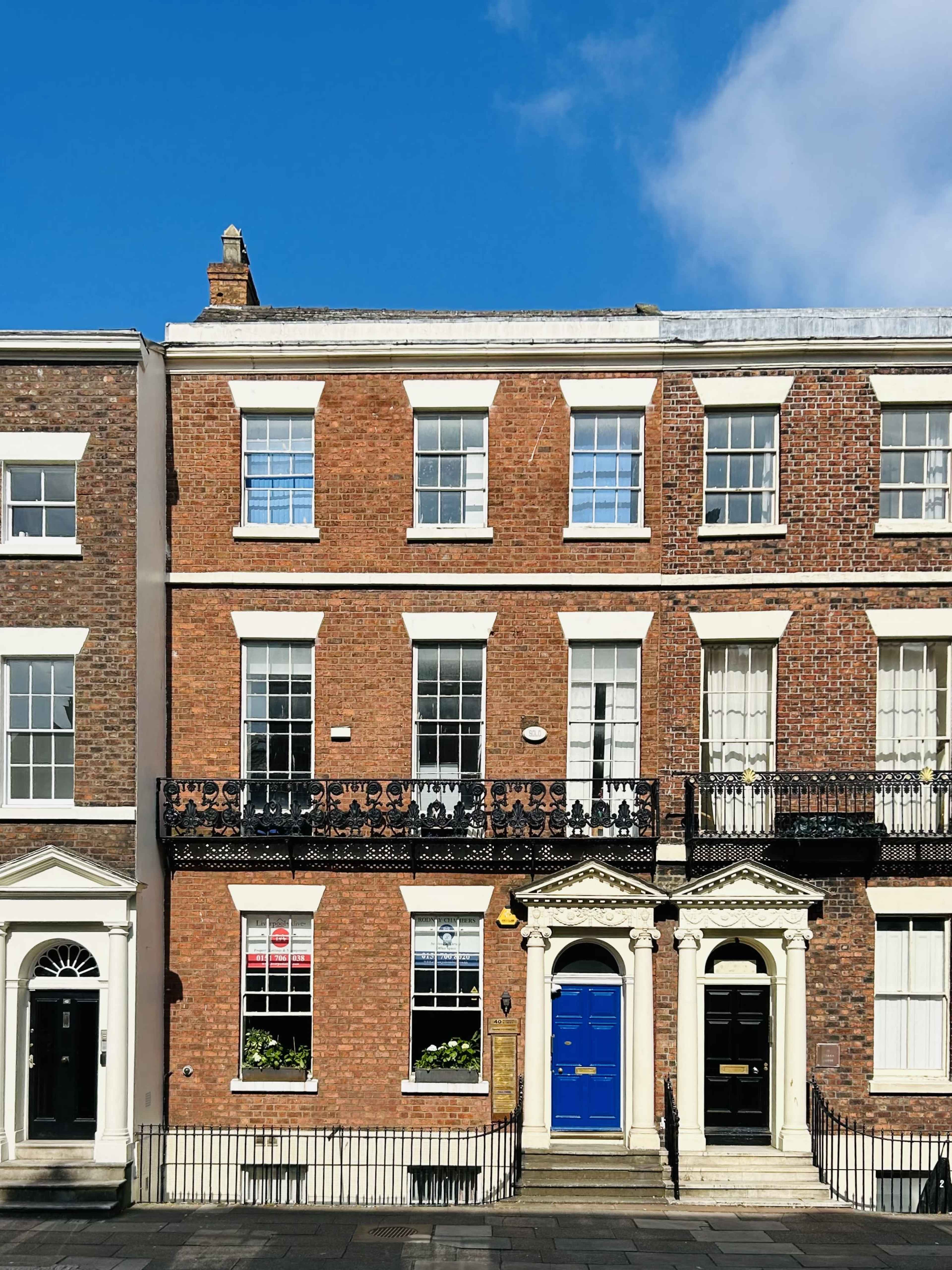 The image shows a row of brick townhouses with white windows and a blue door at the entrance.