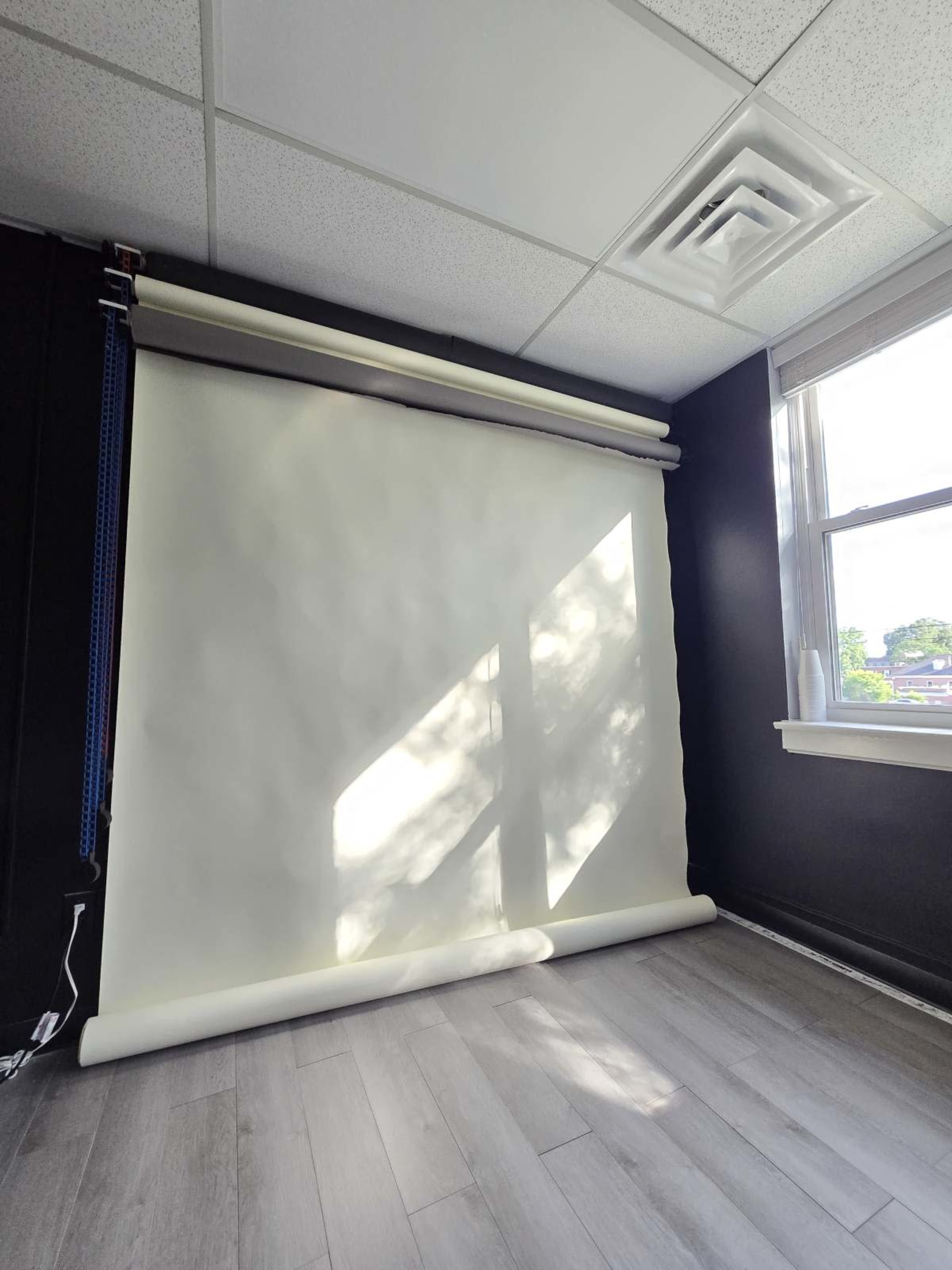 A white backdrop is rolled down against a dark wall in a room with a window, allowing natural light to cast shadows.