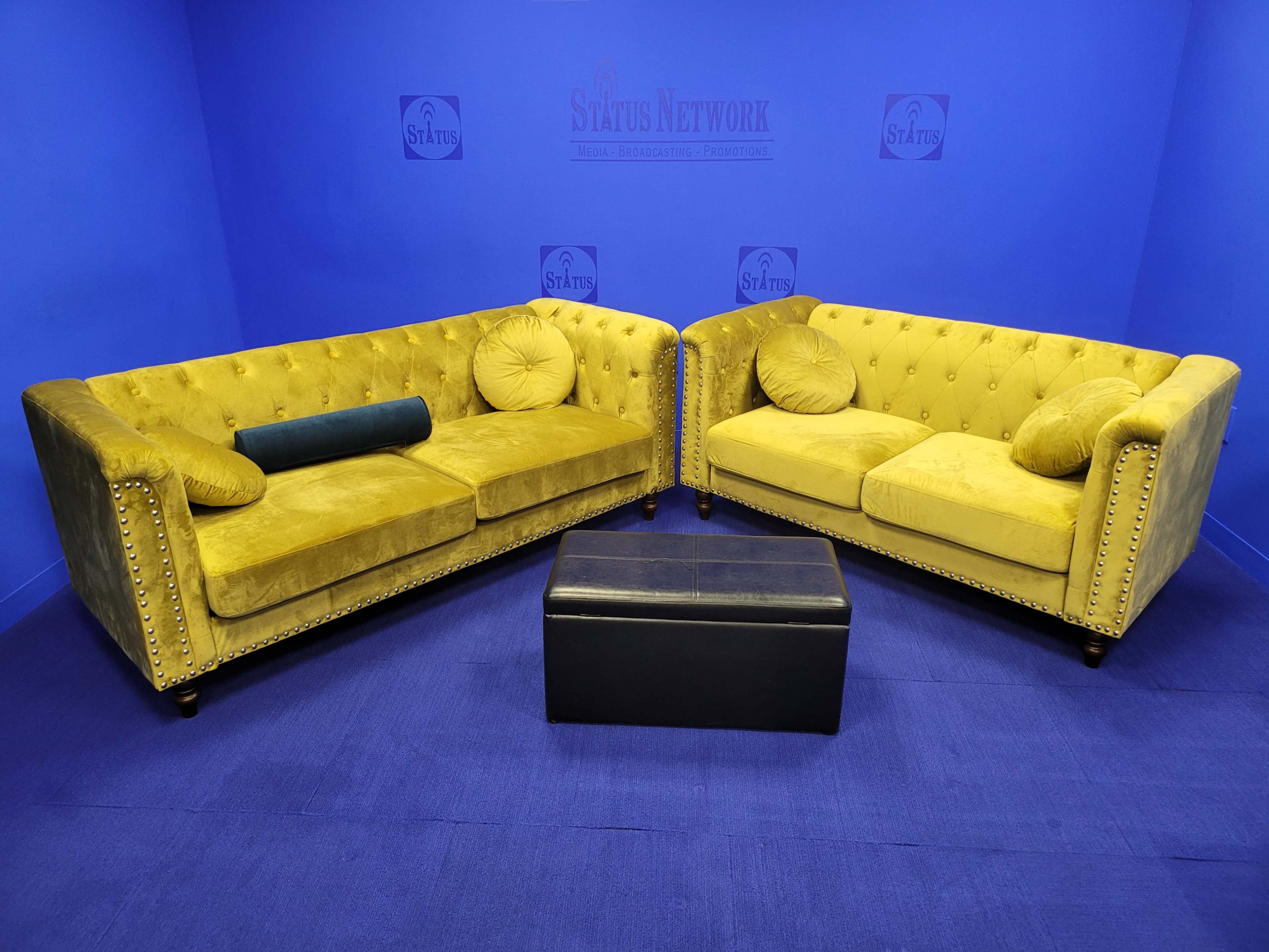 Two yellow tufted sofas facing each other on a blue carpet, with a black coffee table in the center.