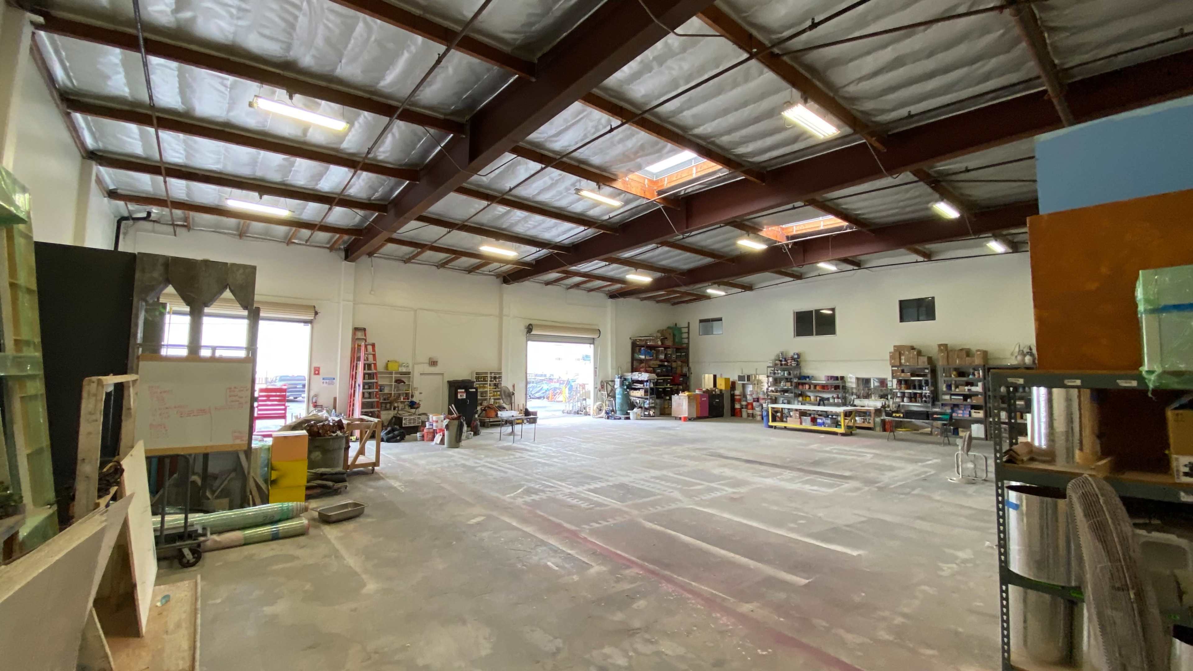 The image shows a spacious warehouse interior with a high ceiling, shelves filled with various items, and a wide open floor area.