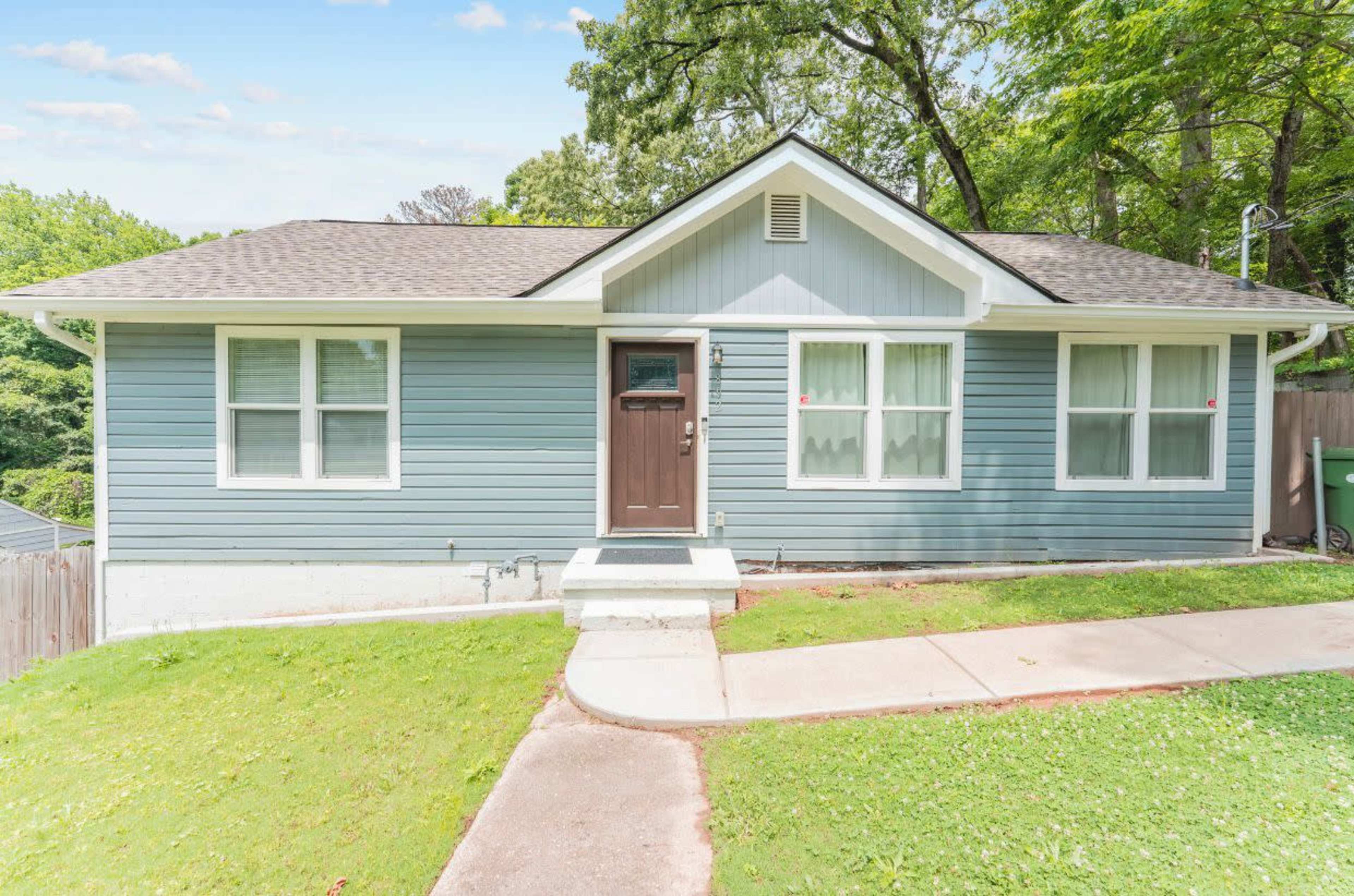 A single-story, blue-painted house with a front porch and well-maintained lawn.