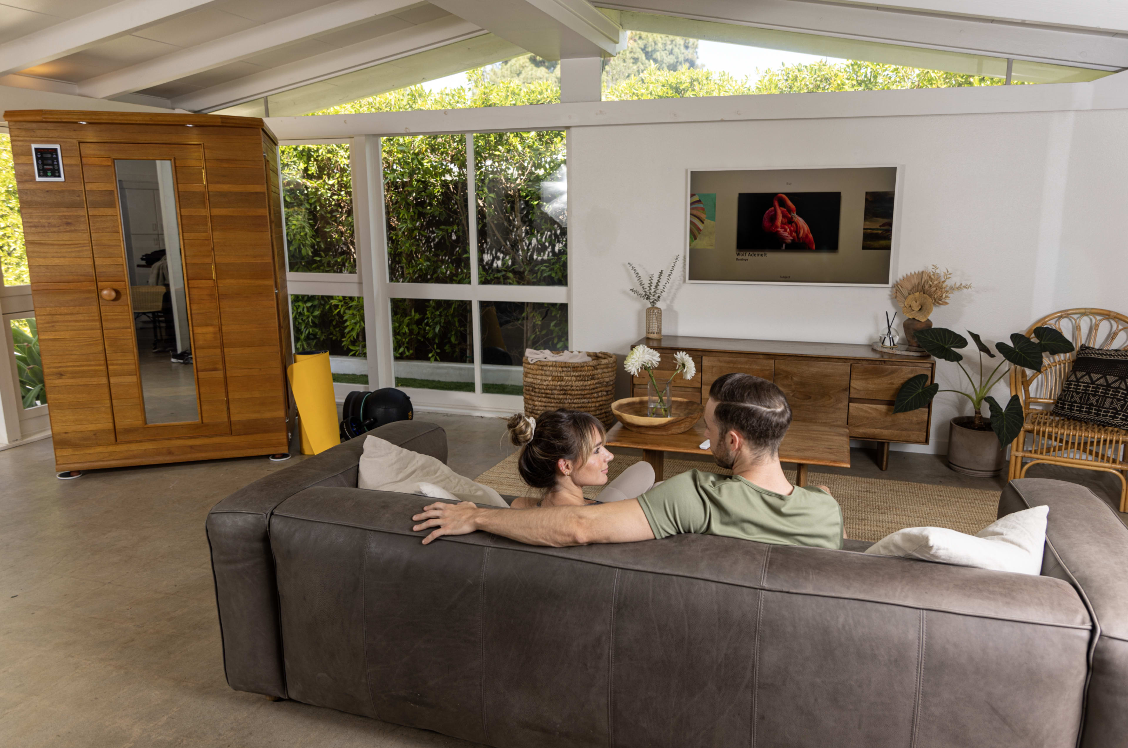 A couple on a brown couch surrounded by plants in a boho living room.