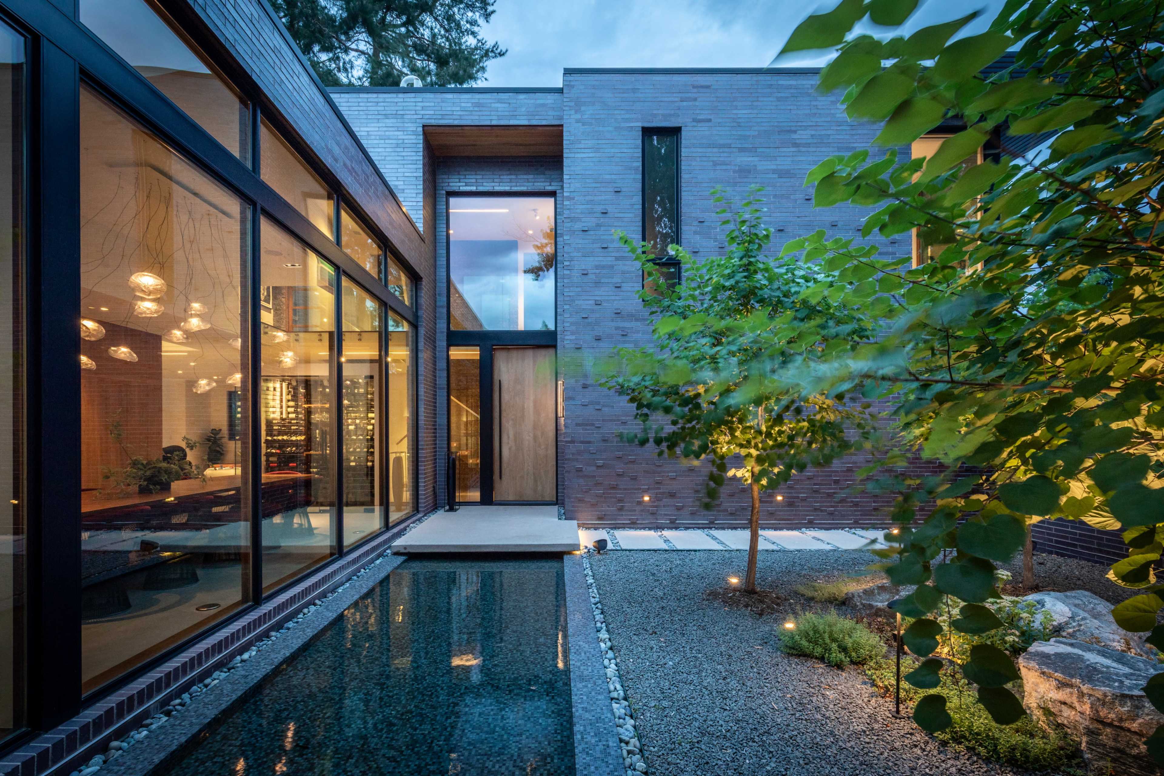 The image shows a modern house with large glass windows, a reflecting pool, and landscaped greenery in the surrounding area.