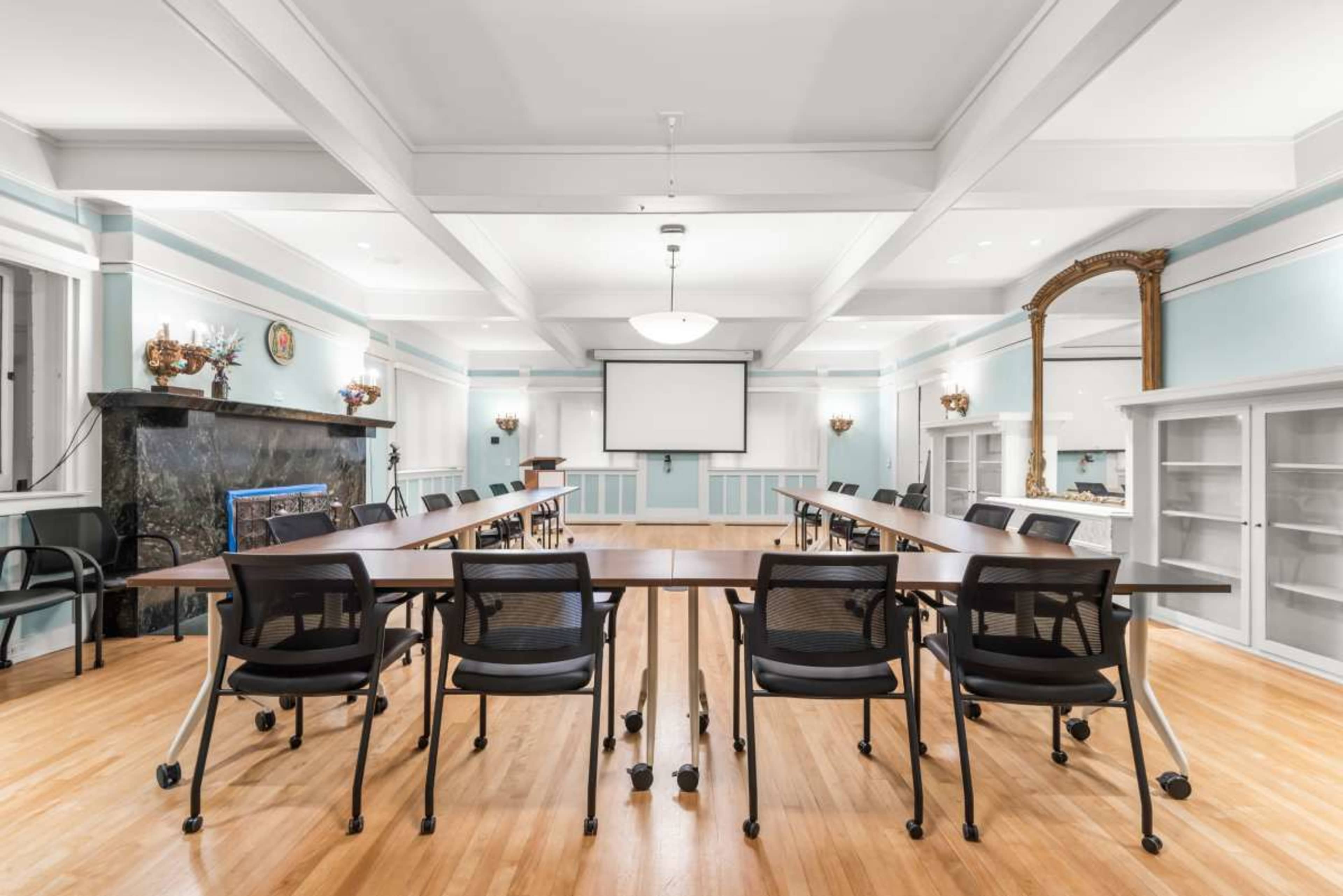 The image shows a spacious conference room with a long table surrounded by black chairs, a projector screen, and large windows.