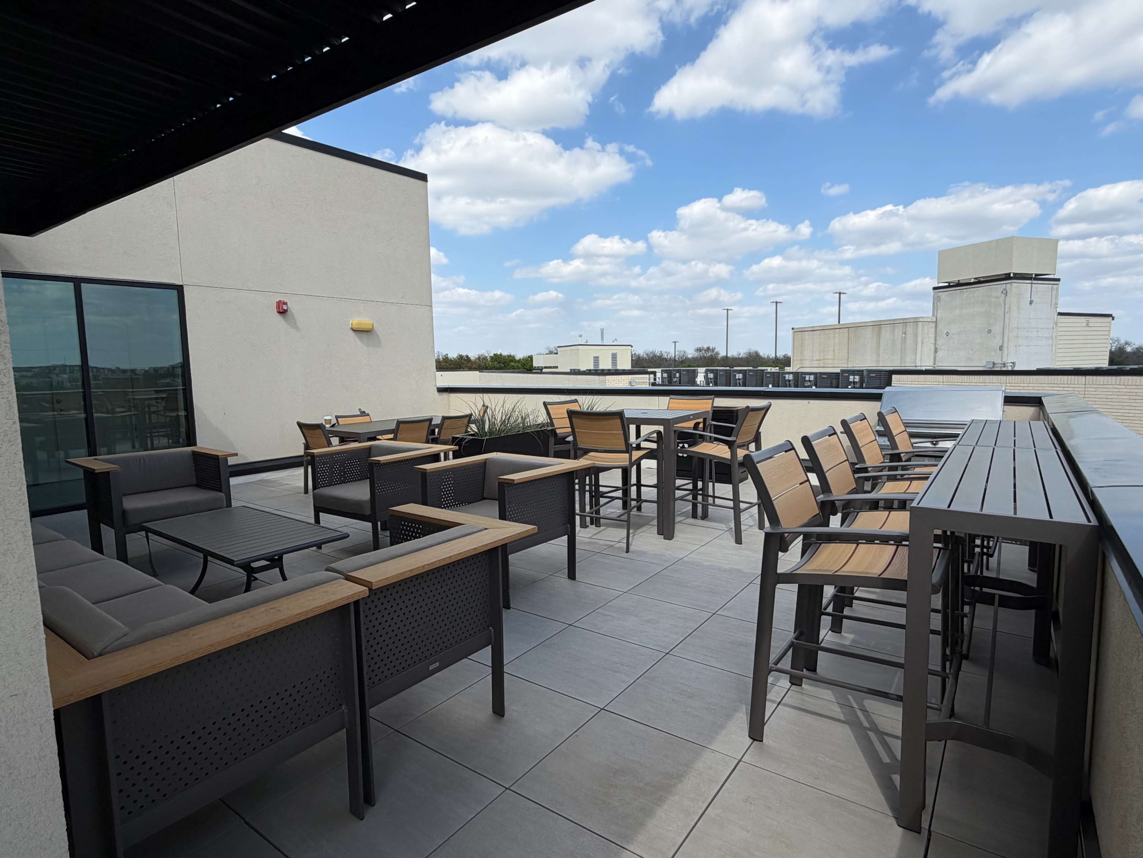 The image shows a rooftop terrace with modern outdoor furniture, including tables and chairs, under a partly cloudy sky.