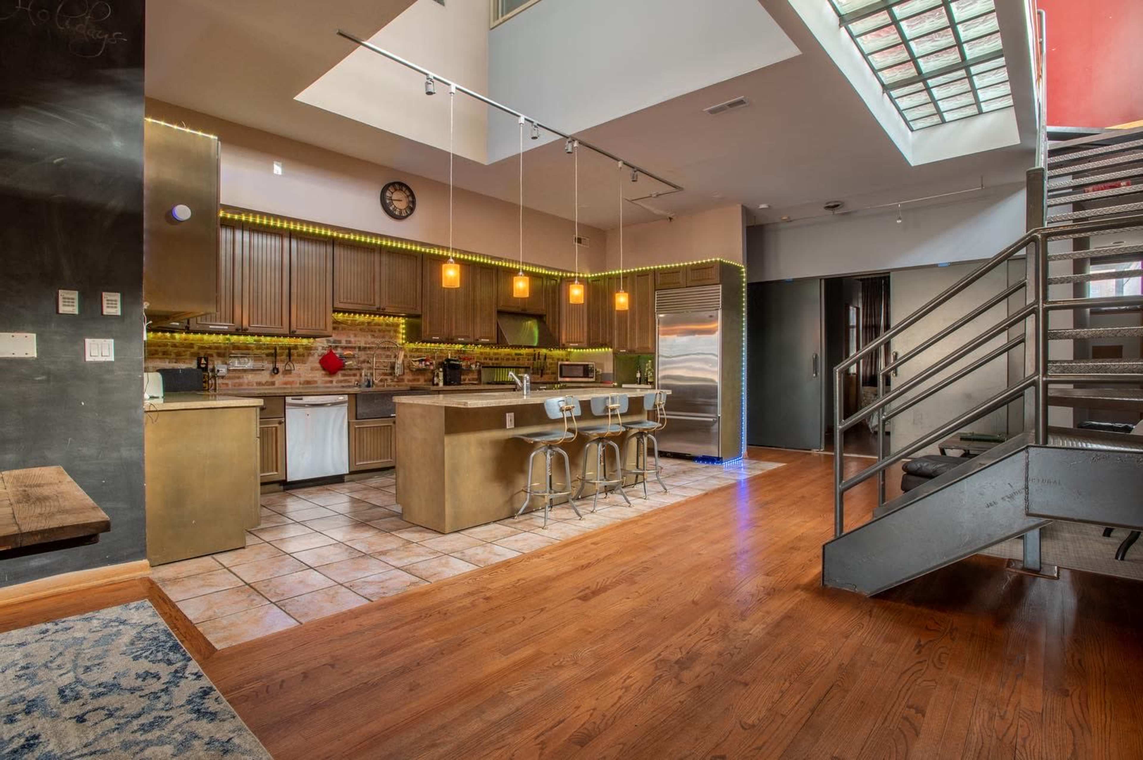 A modern kitchen with stainless steel appliances, a central island with seating, and a staircase leading to an upper level.