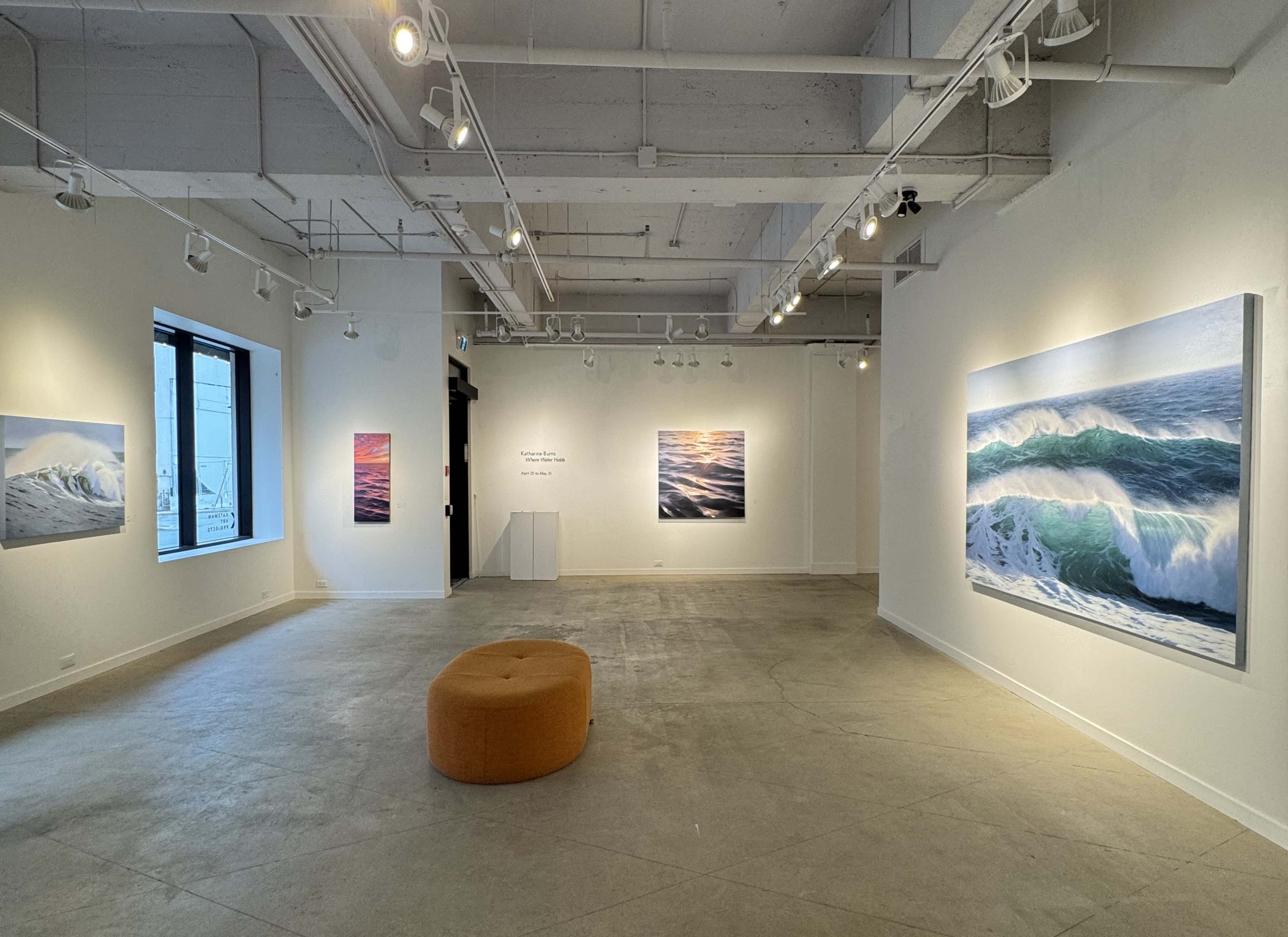 The image shows an art gallery with large wave paintings displayed on the walls and a circular orange seating area in the center.