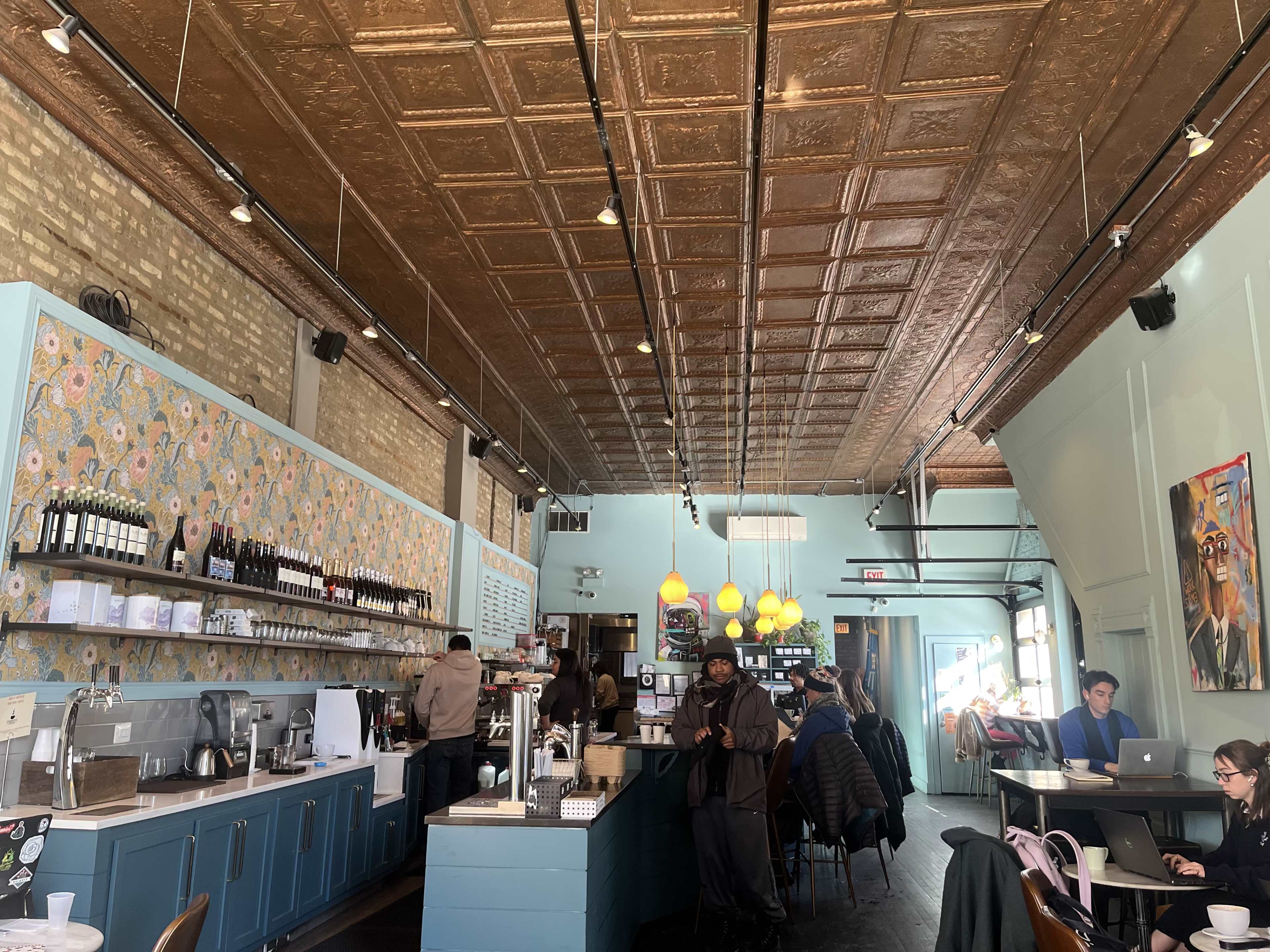 The image shows a cafe interior with a blue counter, patterned walls, and customers seated at tables.
