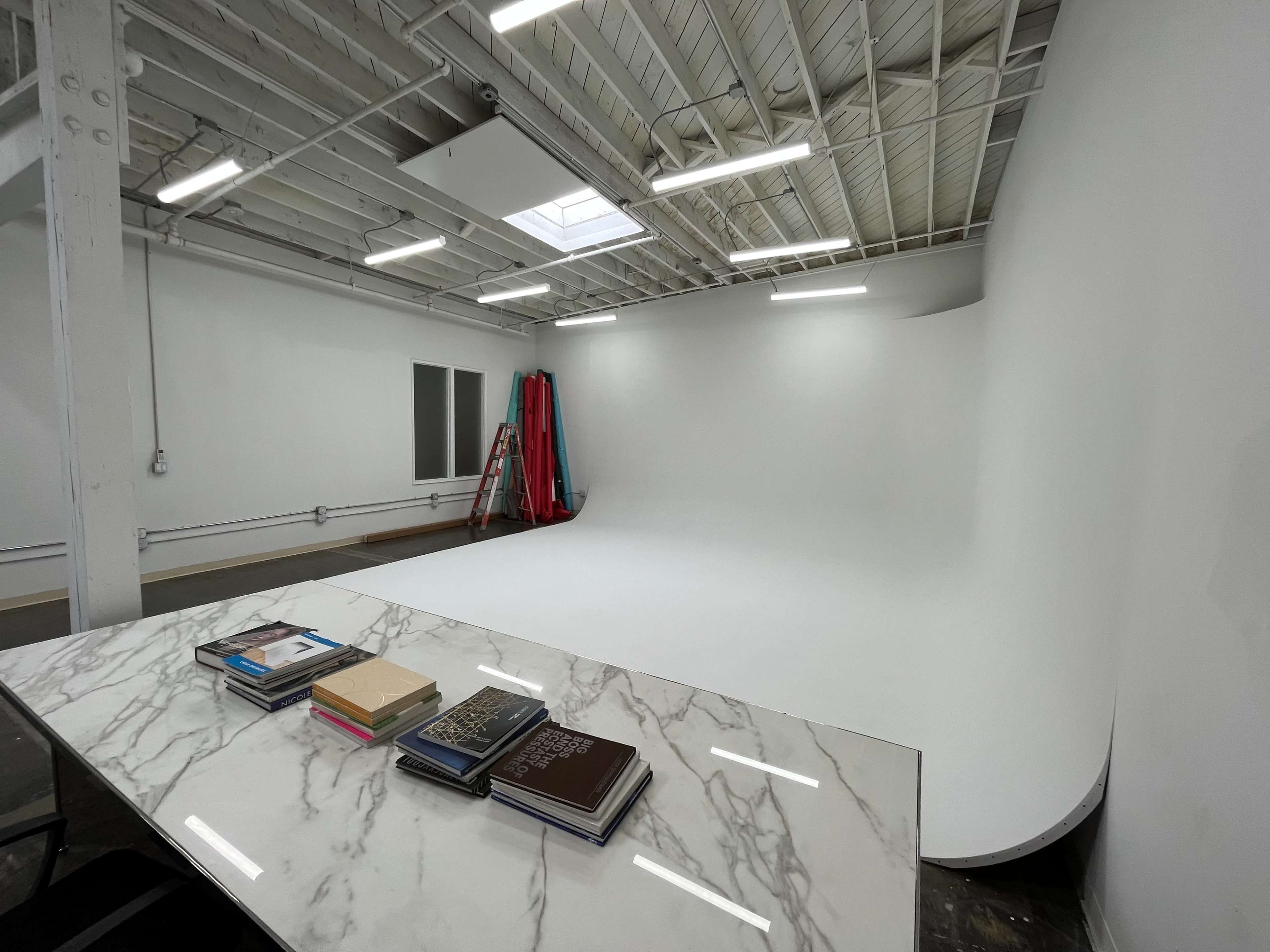 The image shows a spacious, well-lit studio with a curved white backdrop and a marble table displaying several stacked books.