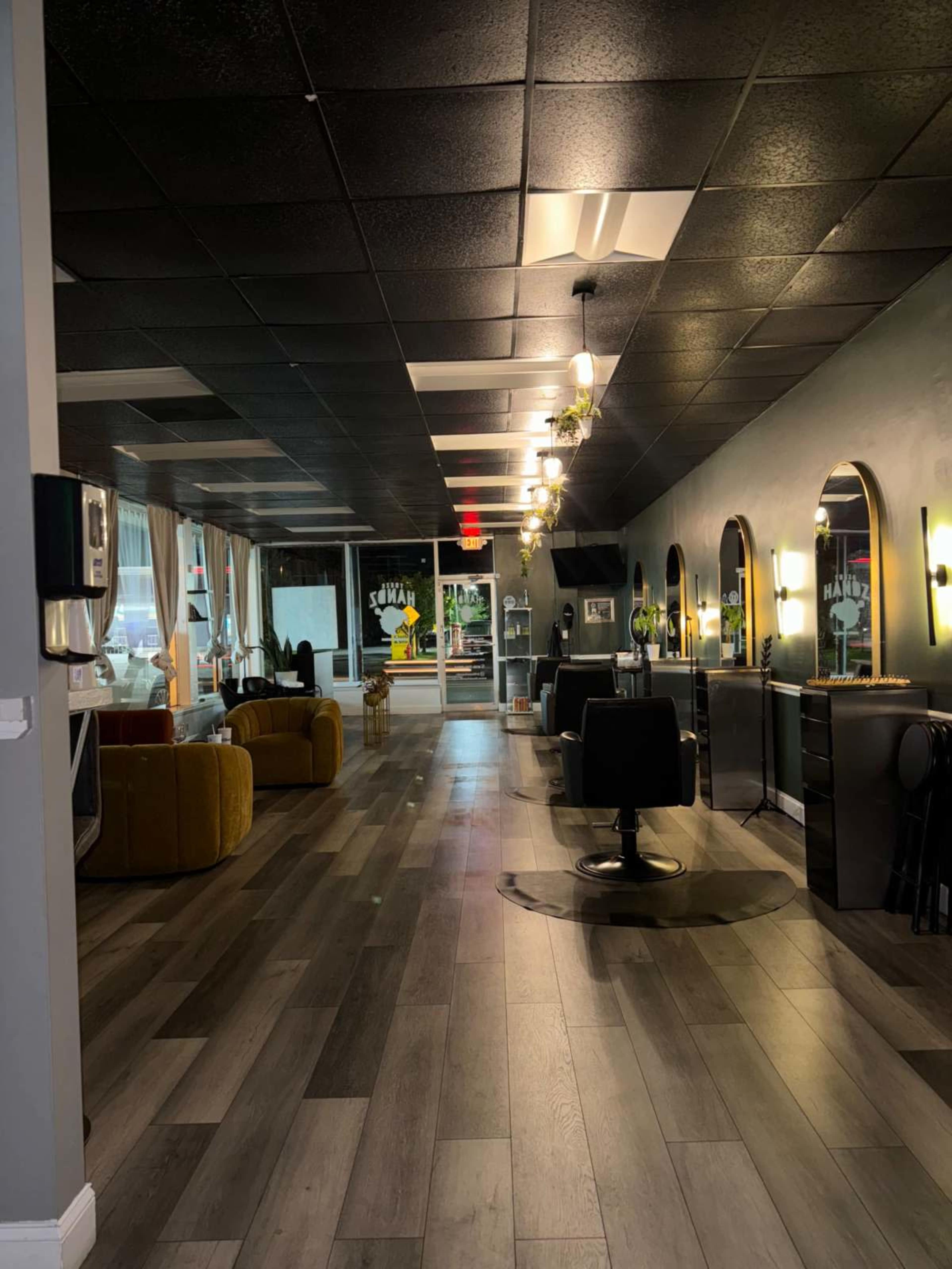 The image shows a spacious, modern hair salon featuring styling stations, two comfortable seating areas, and large mirrors along one side.