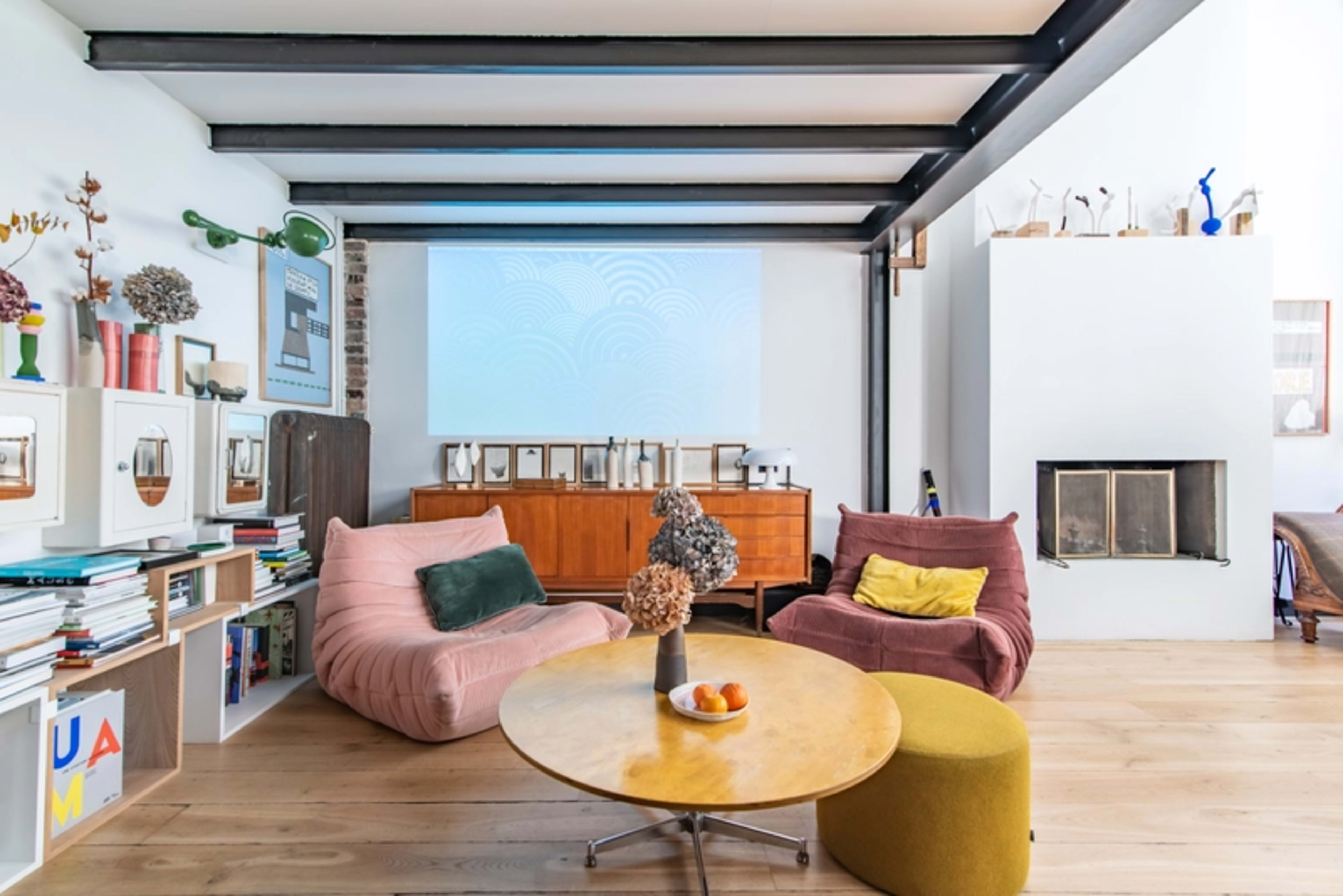 A modern living room with two bean bag chairs, a round coffee table, and a large projection screen on the wall.