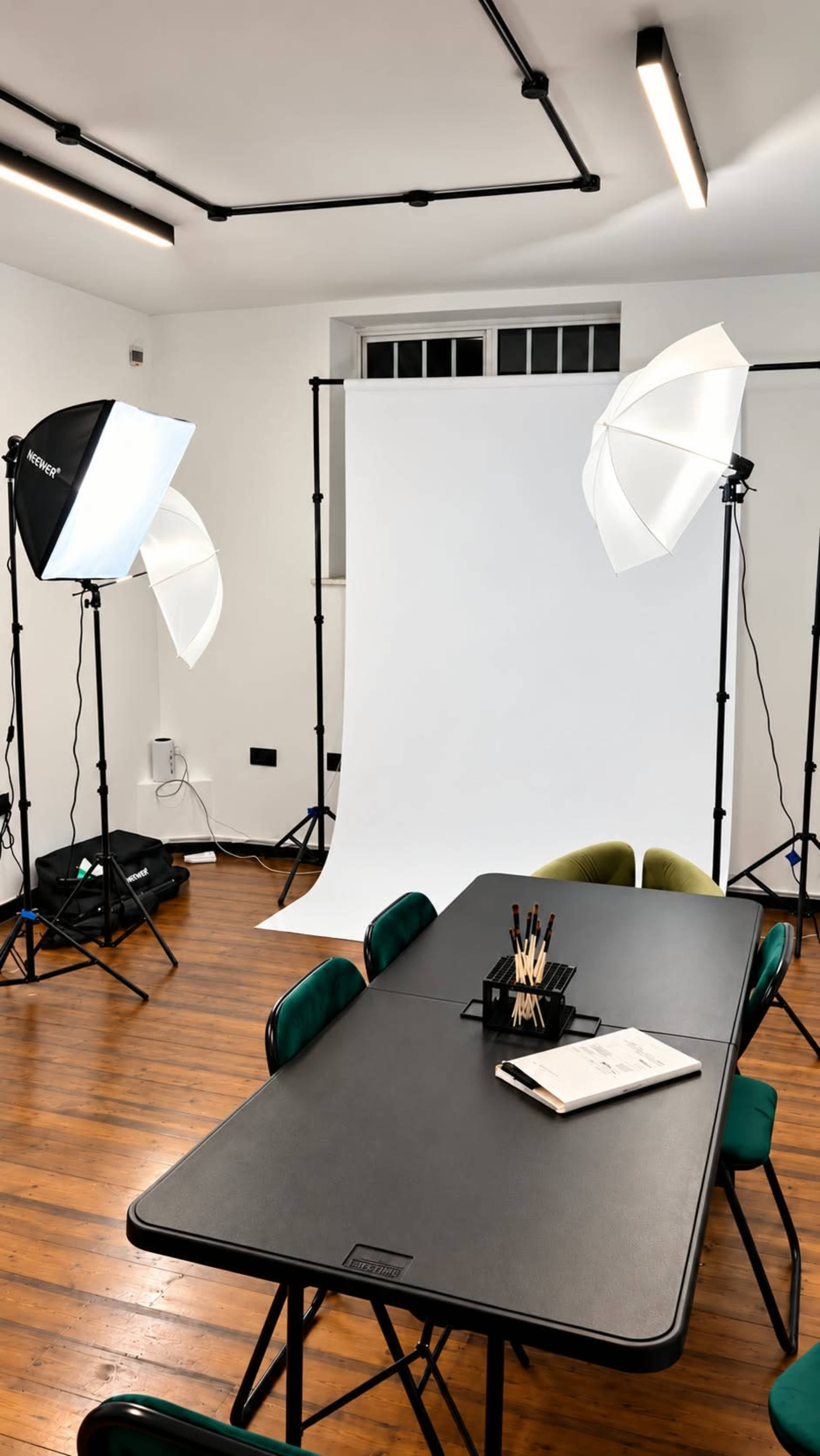 A well-lit photography studio features a large backdrop, two softbox lights, and a table equipped with stationery.
