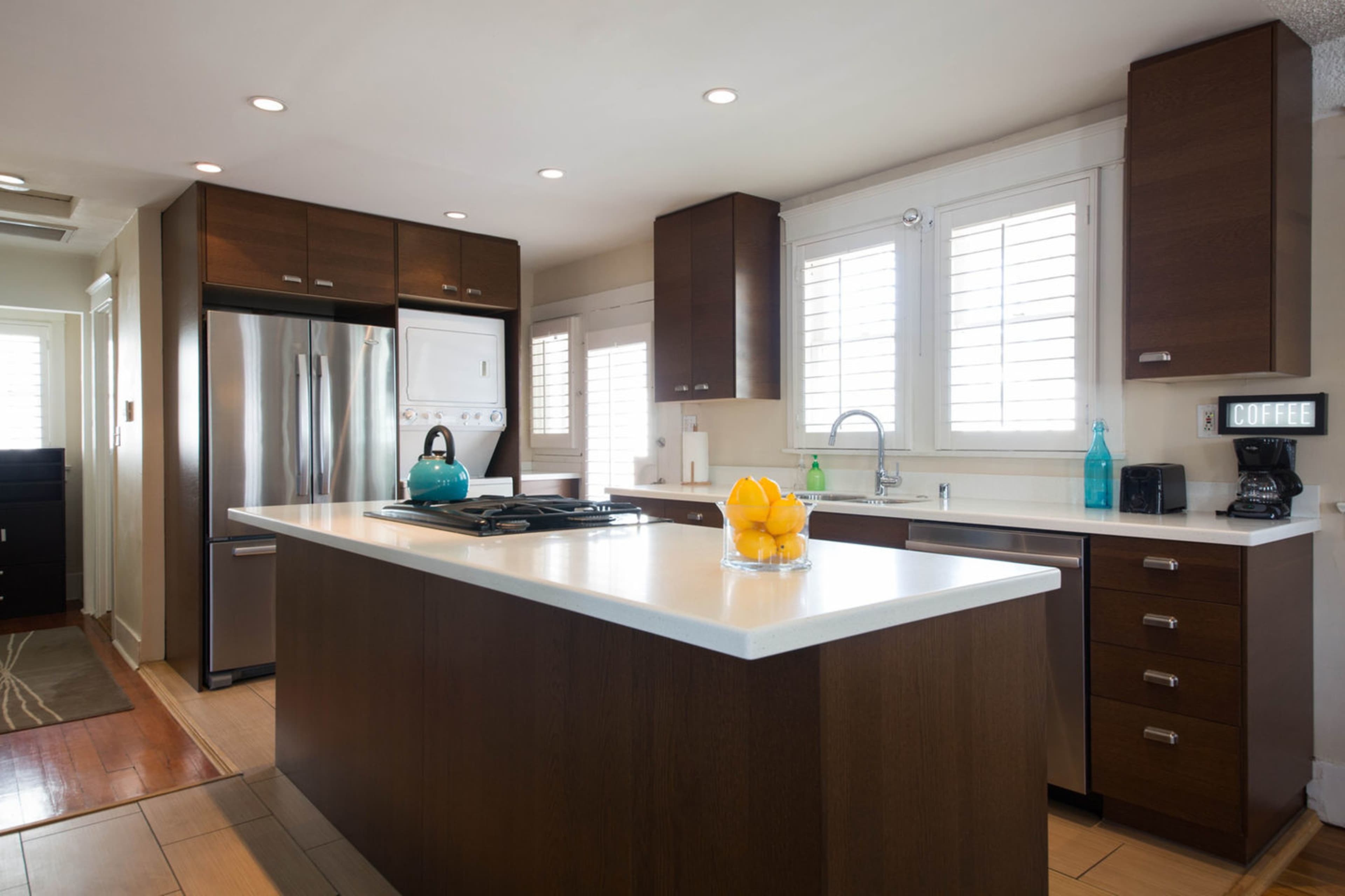 A modern kitchen featuring dark wood cabinetry, a central island with a white countertop, and stainless steel appliances.