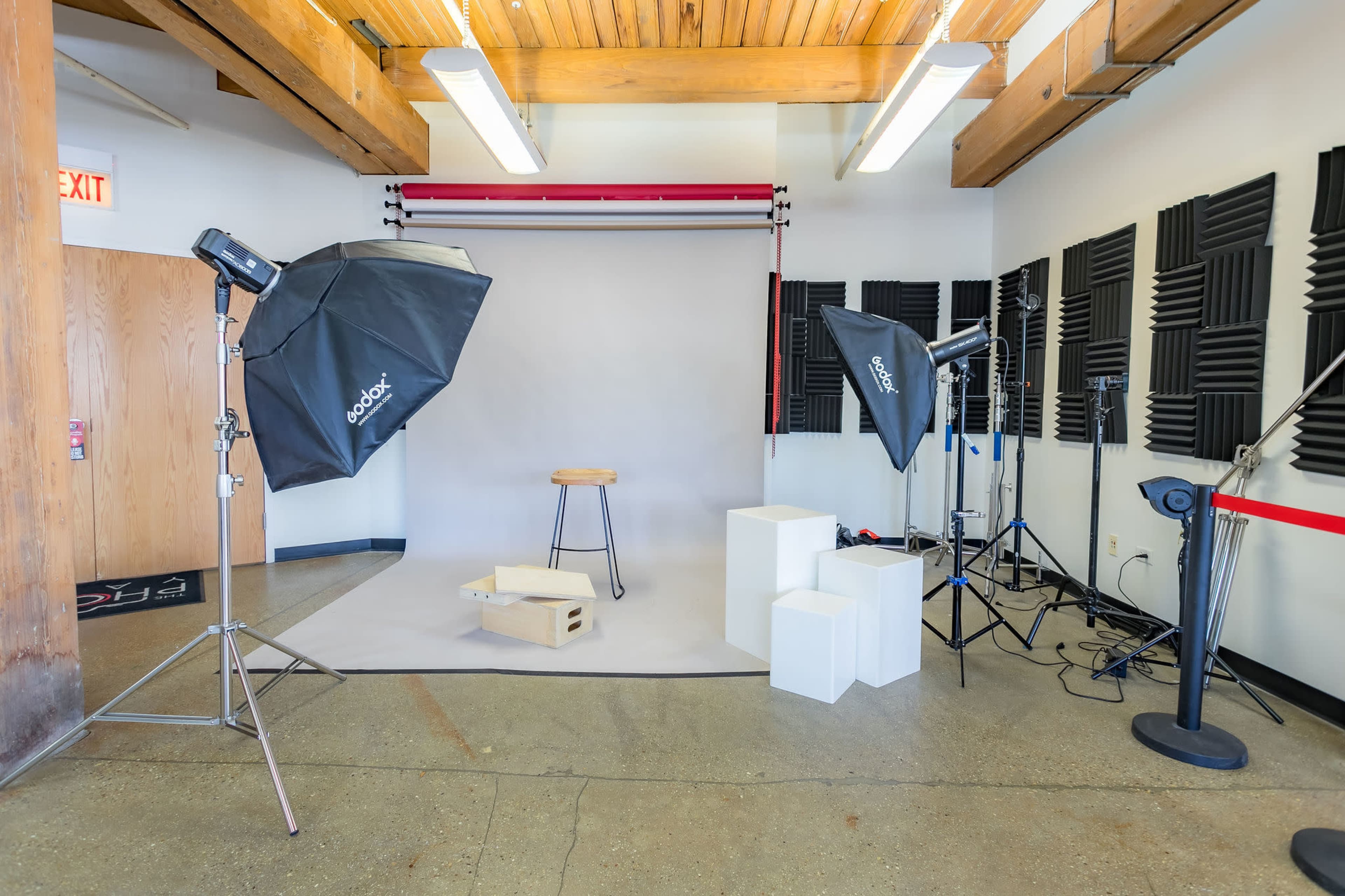A photography studio is set up with softbox lighting, a backdrop, a stool, and white display blocks.