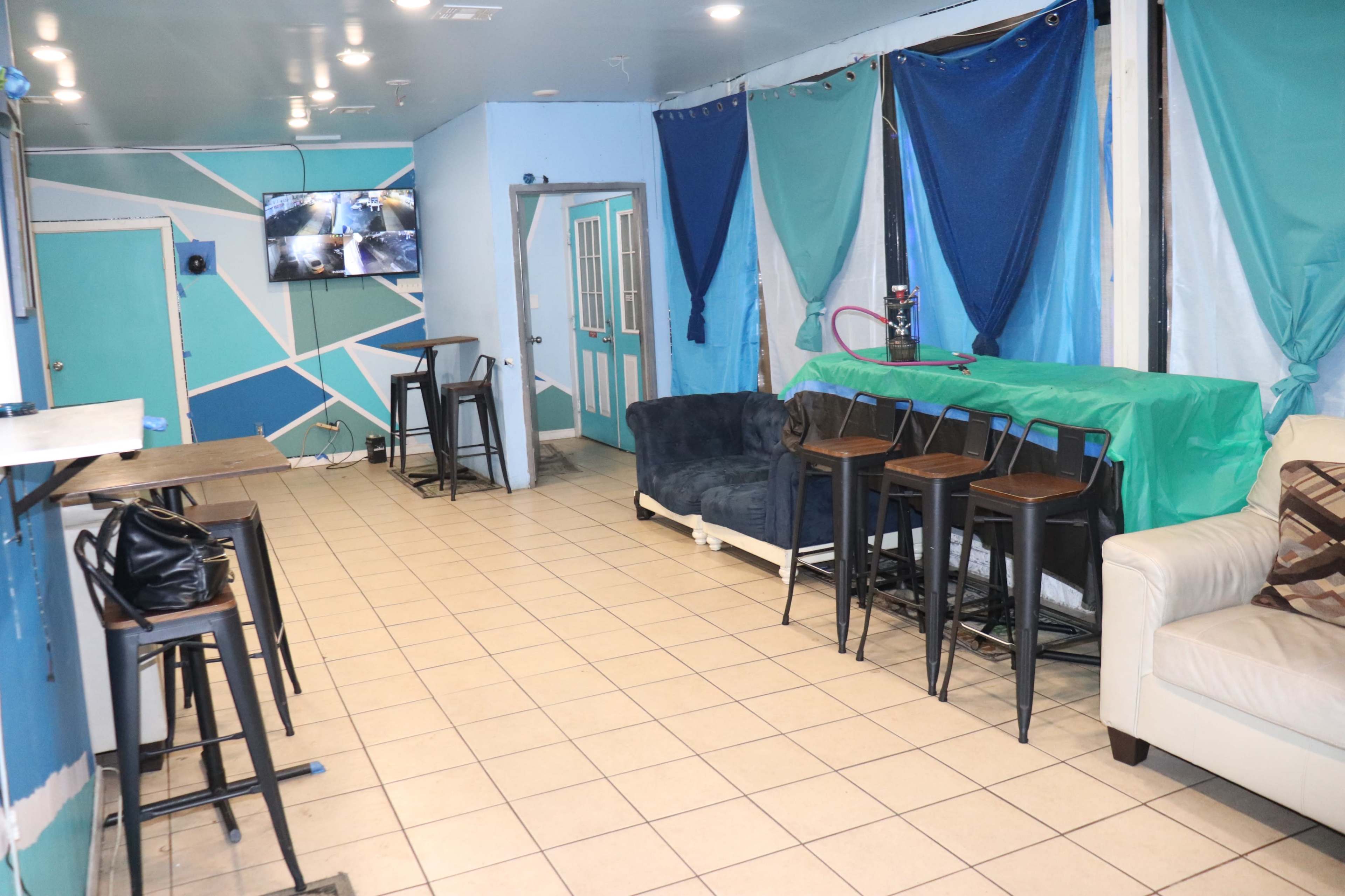 A room with a tiled floor containing several seating areas, a bar with stools, and a wall-mounted TV.