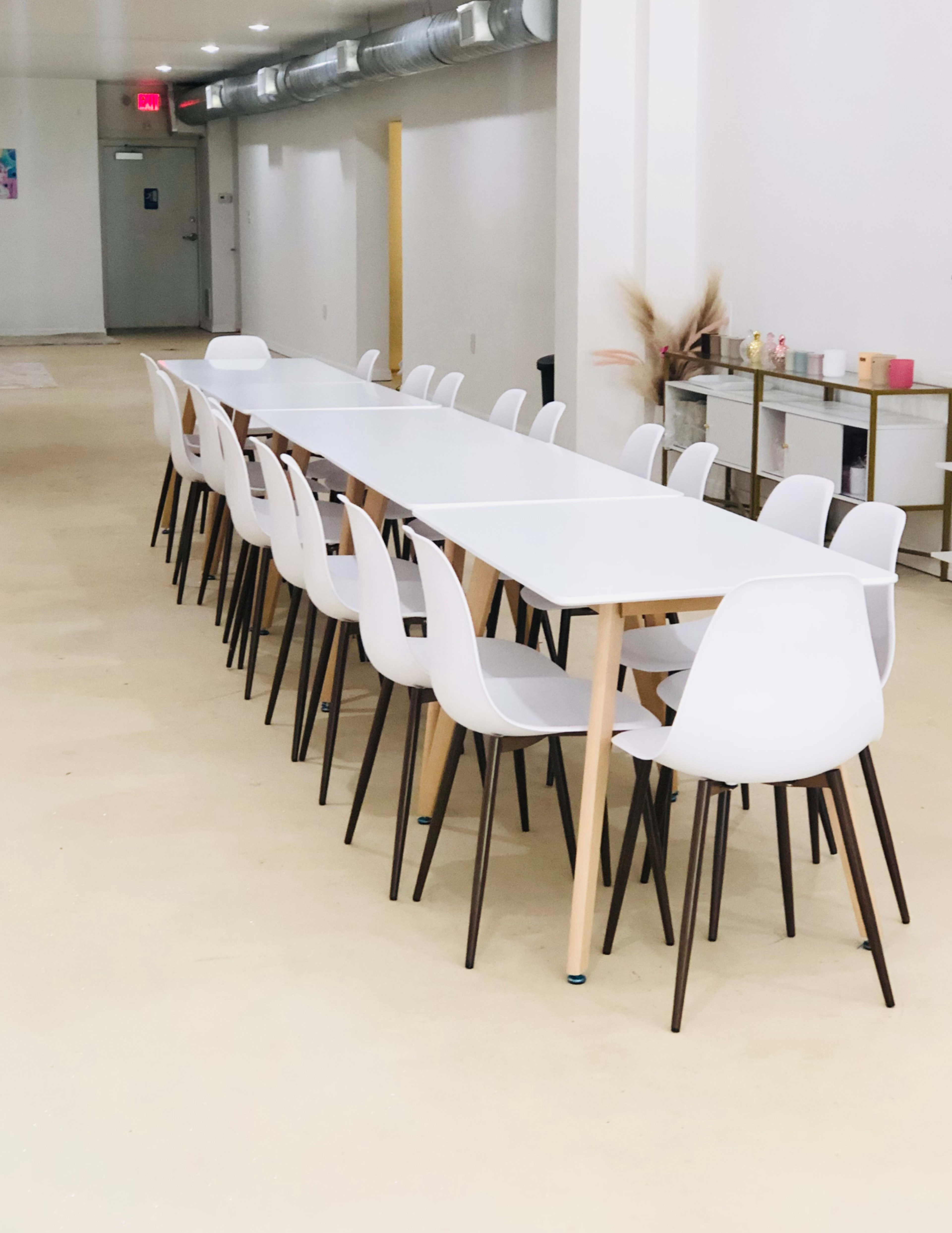 A long, white table is set with white chairs arranged neatly in a spacious, well-lit room.